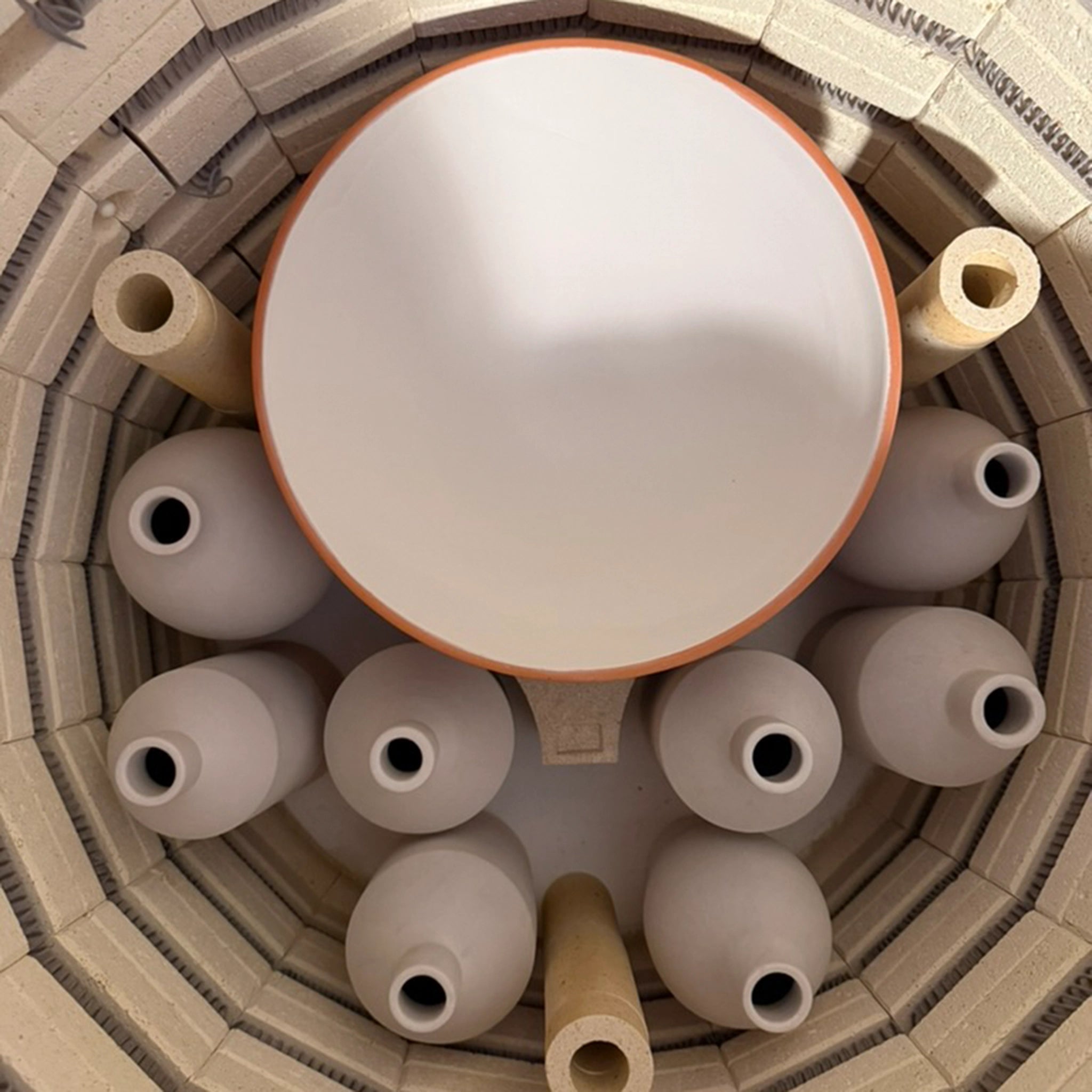 Een bovenaanzicht in een oven toont verschillende handgedraaide, ongeglazuurde vazen en de AB Ceramics Olijfolie Fles Grijs Opaal 84 cl op ovenplanken - ideaal voor het maken van unieke keukenaccessoires van AB Ceramics.