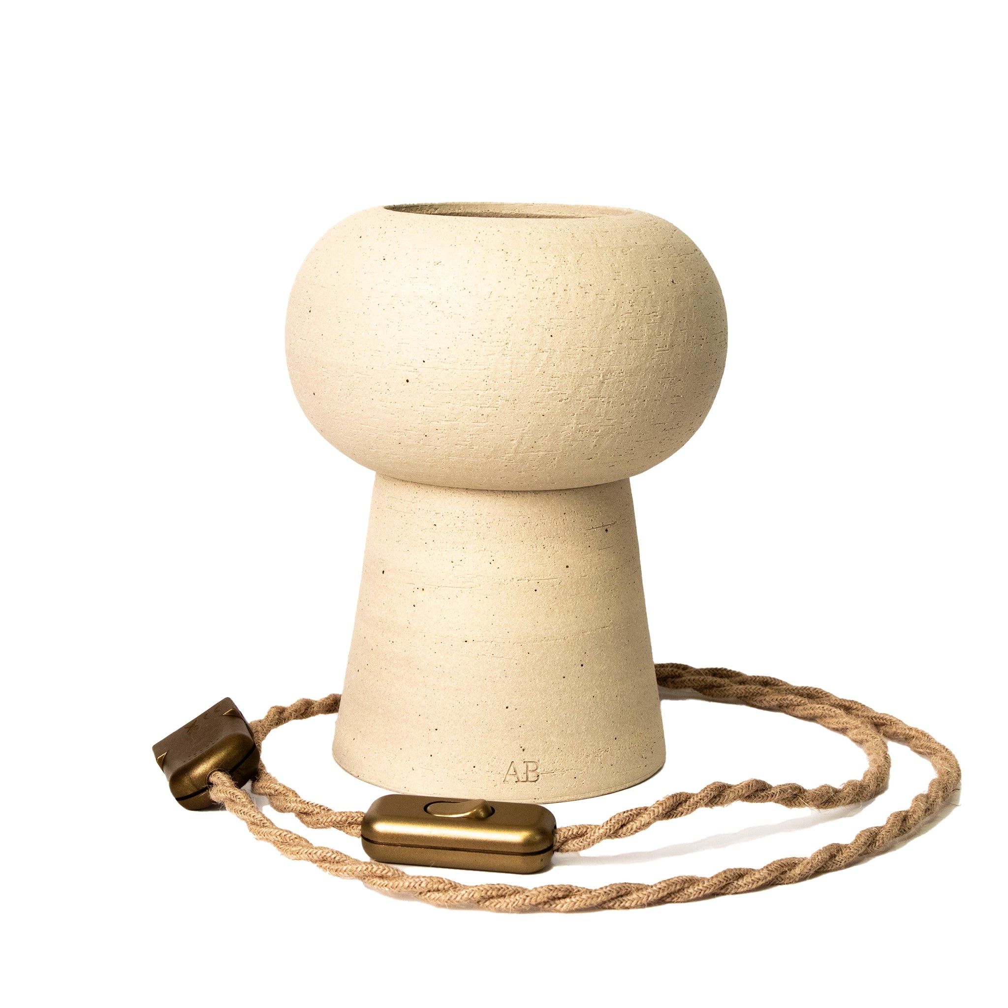 De AB Ceramics Sfeerlamp 20cm is een handgemaakte beige keramieken lamp met afgeronde bovenkant, conische basis en gedraaide bruine elektradraad met gouden schakelaar van het merk AB Ceramics.