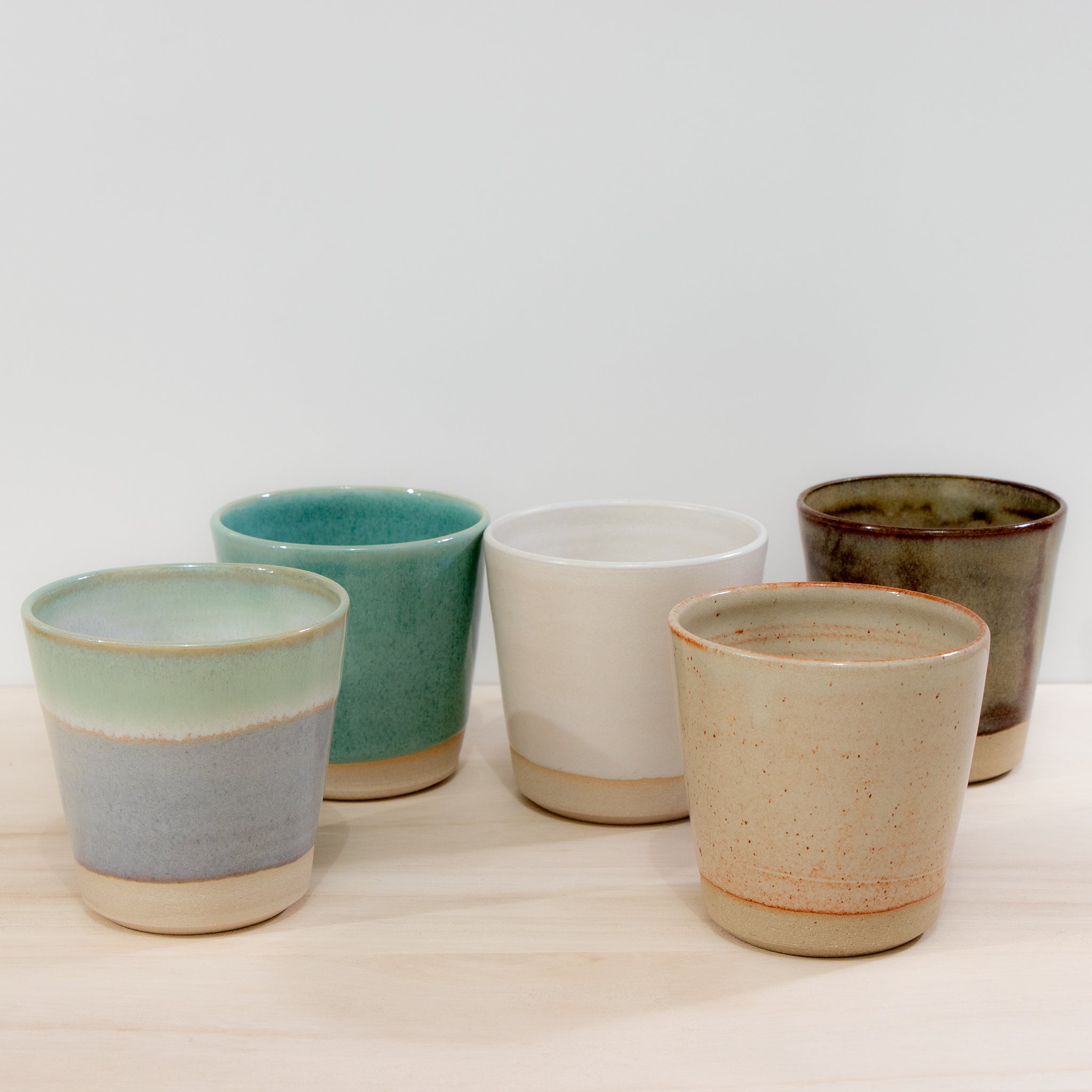 De AB Ceramics Beker Geel Beige 20 cl van AB Ceramics is een handgemaakte keramische beker in gele en beige tinten, vervaardigd uit steengoed en stijlvol gepresenteerd op een licht houten oppervlak tegen een witte achtergrond.