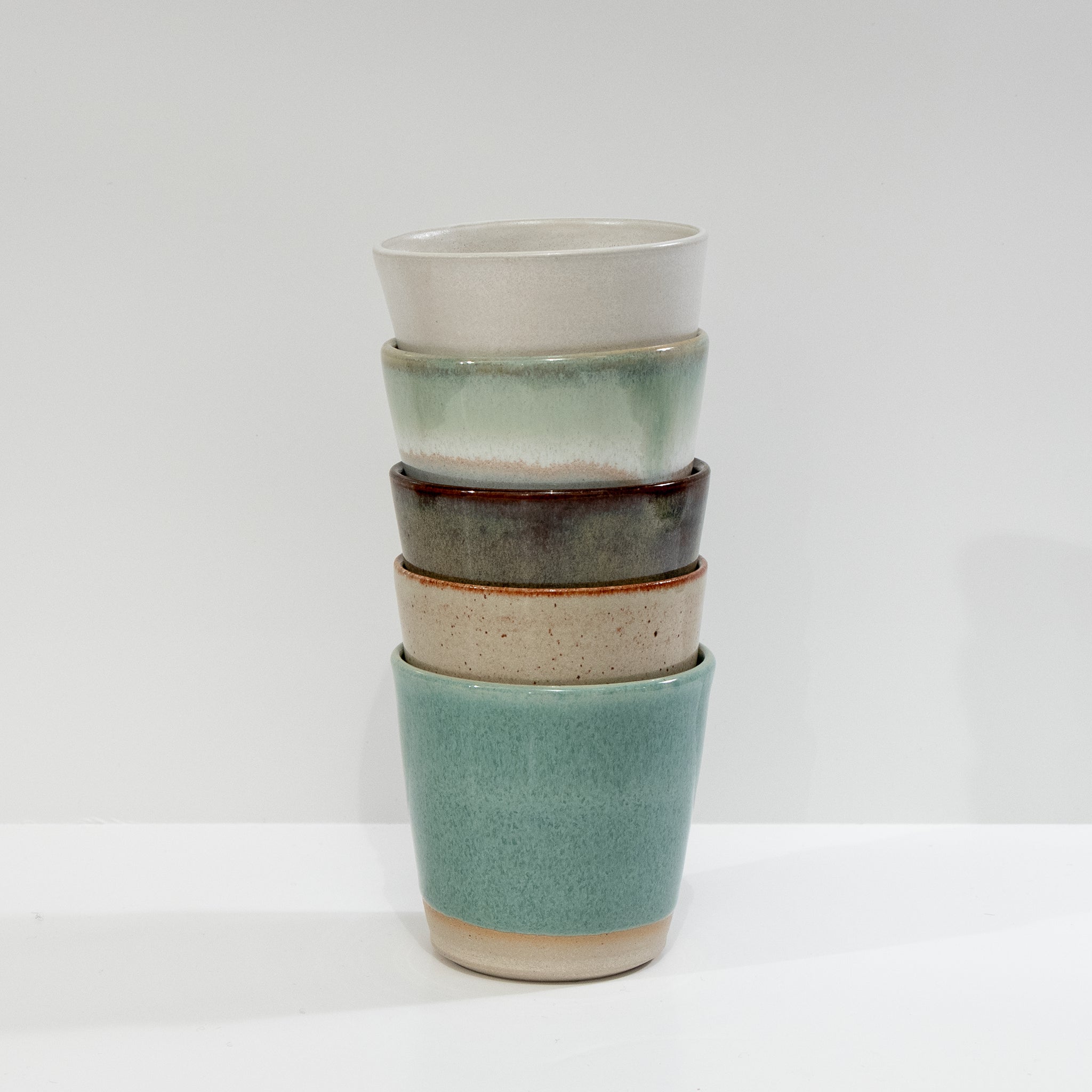 Vier handgemaakte AB Ceramics bekers van steengoed, 20 cl, in geel, roodbruin en beige met uniek glazuur, gestapeld tegen een witte achtergrond.