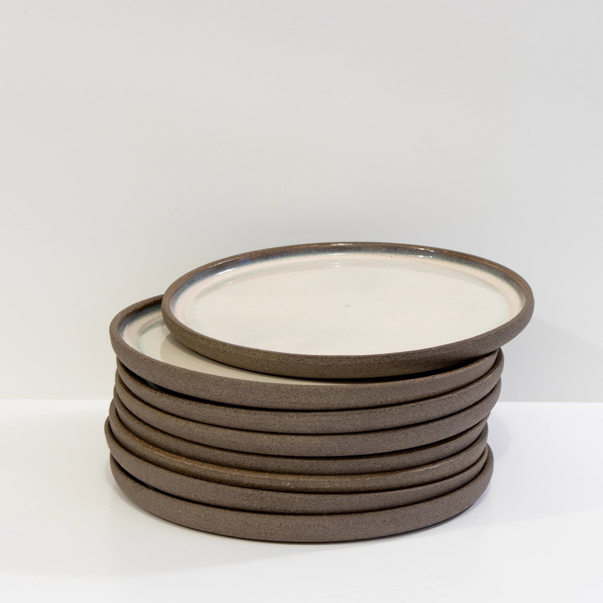 Een stapel van acht AB Ceramics Laag Bord Antraciet Opaal D19,5 ronde borden met bruine randen en glanzend wit midden, op een effen witte achtergrond. Het bovenste bord is licht gekanteld en rust op de stapel.