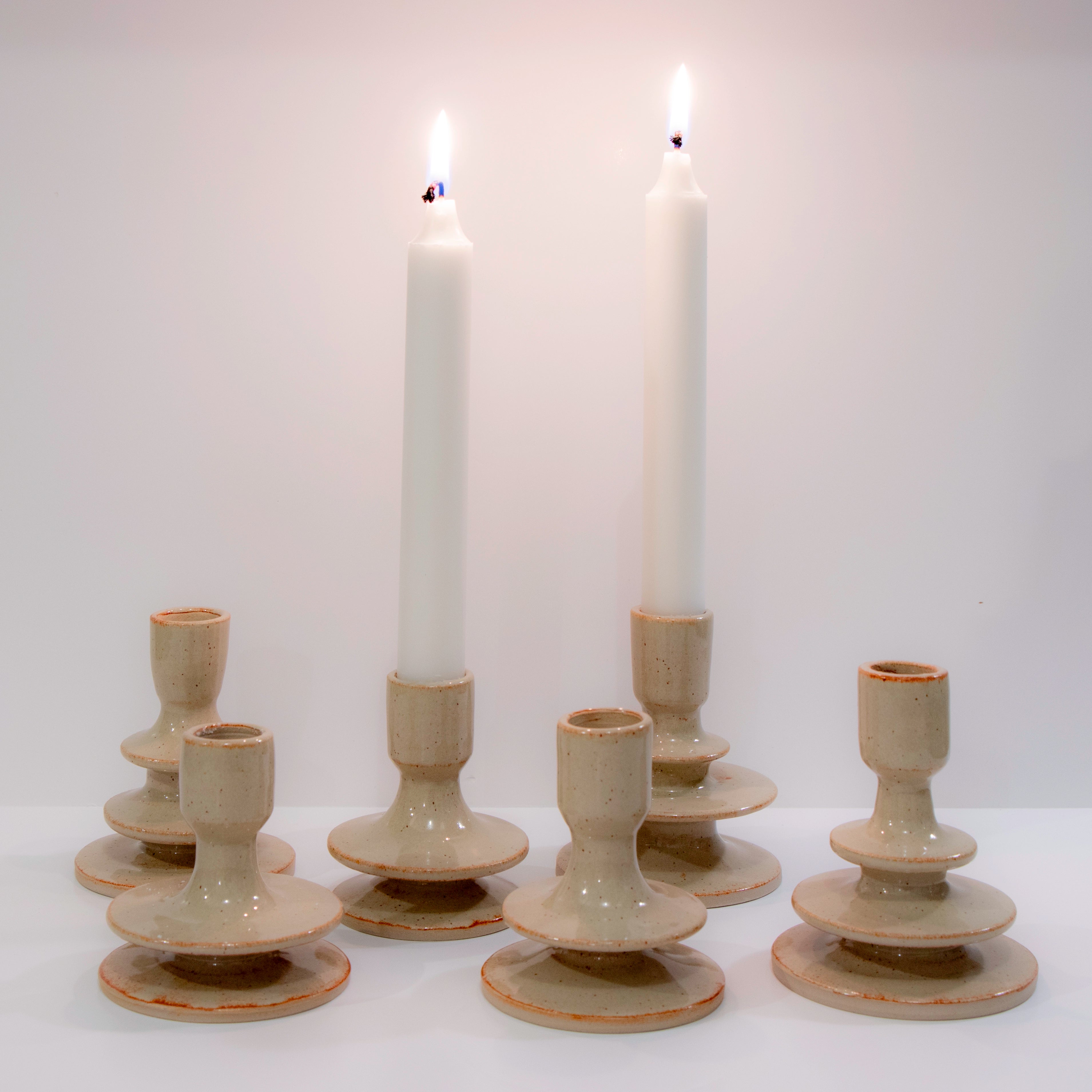 Zes AB Ceramics Kandelaar Wit Beige 3 lagen kandelaars staan in twee rijen op een wit vlak; twee houden hoge brandende witte kaarsen, terwijl vier leeg zijn. De effen achtergrond houdt de focus op deze stukken van AB Ceramics.