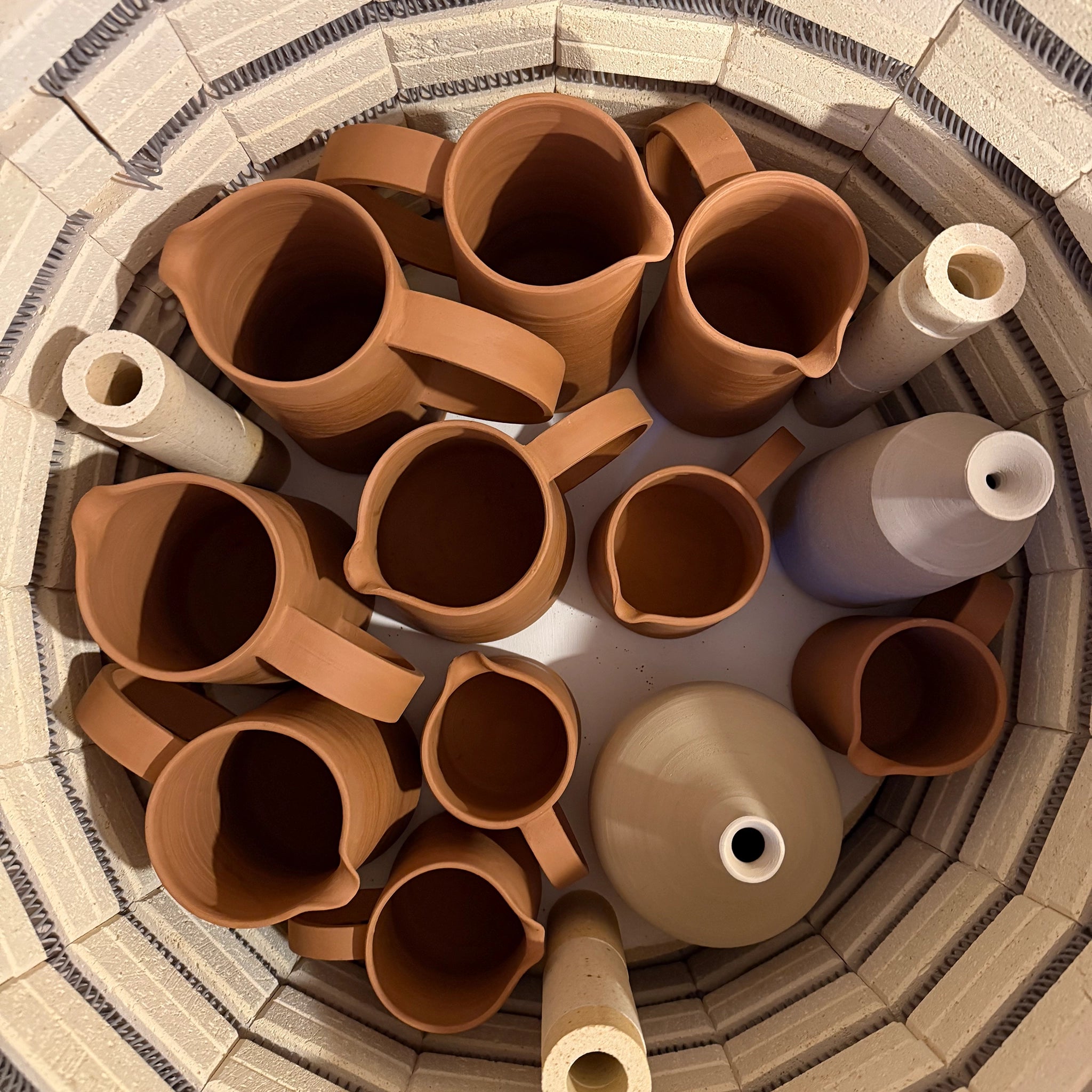 Bovenaanzicht van meerdere AB Ceramics Karaf 6 Rood Opaal Blauw 50 cl van AB Ceramics, opgesteld in een cirkelvormig patroon in een oven, omringd door ovenposten en bakstenen muren.