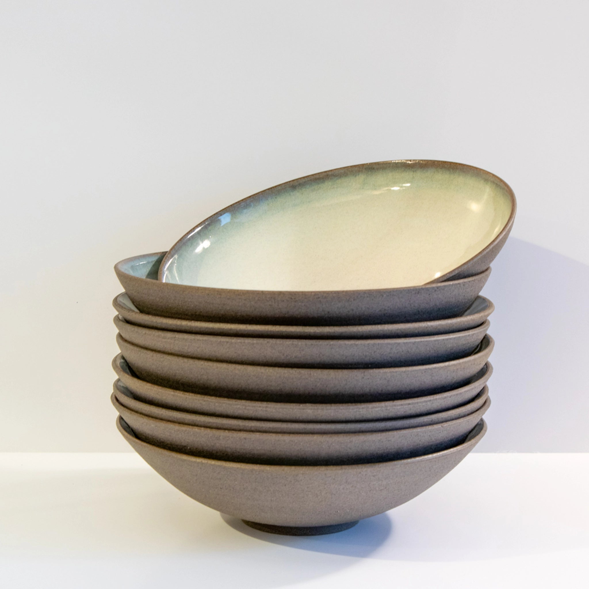 Een stapeltje van zes AB Ceramics Diep Bord Grijs Opaal D21 kommen, met een matbruine buitenkant en een glanzende lichtbeige binnenkant, zijn netjes gerangschikt op een wit oppervlak tegen een effen witte achtergrond.