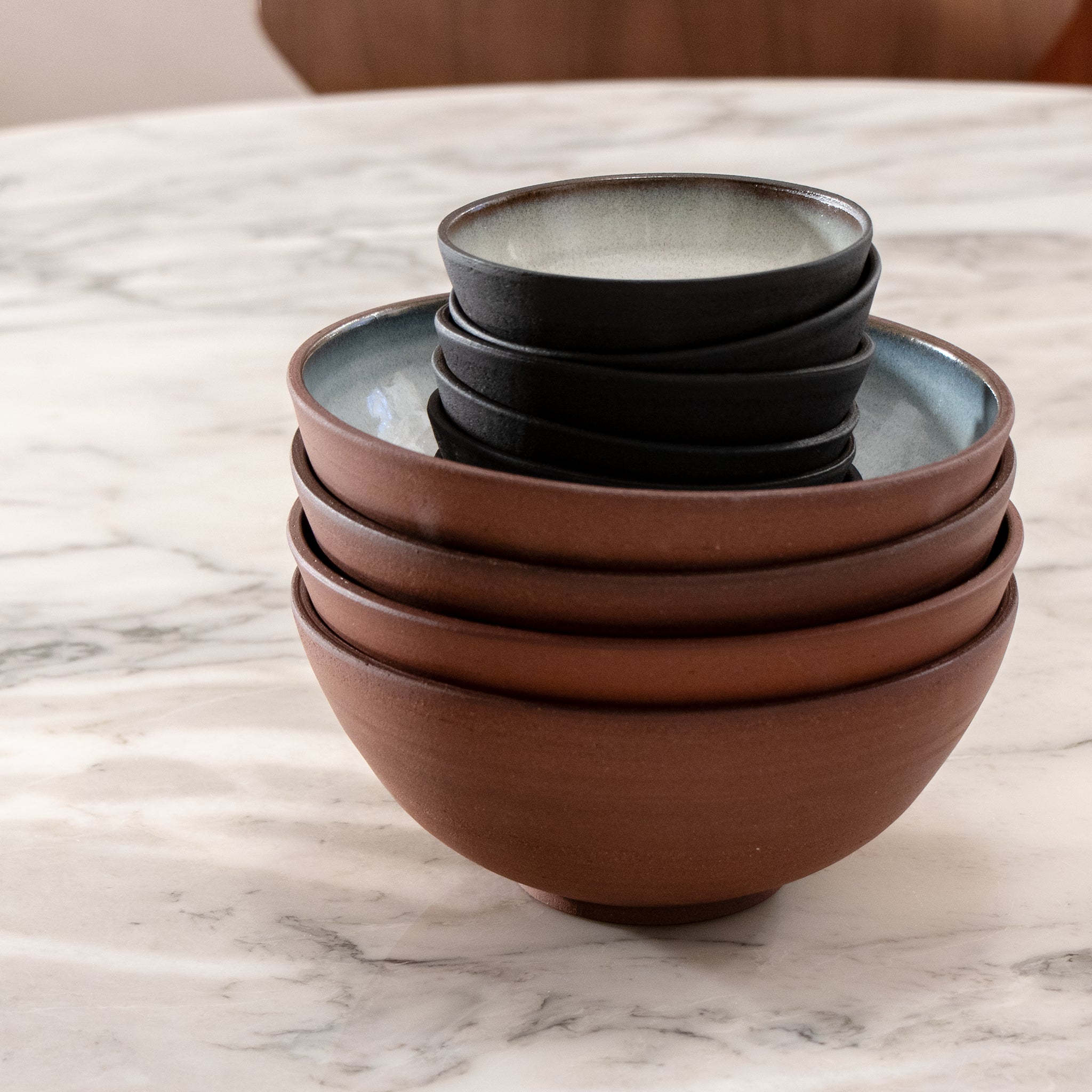 Een stapel van vier Kom Rood Opaal D18 kommen van AB Ceramics, elk met een kleinere donkere noedelkom erin genesteld, geplaatst op een wit marmeren tafelblad.