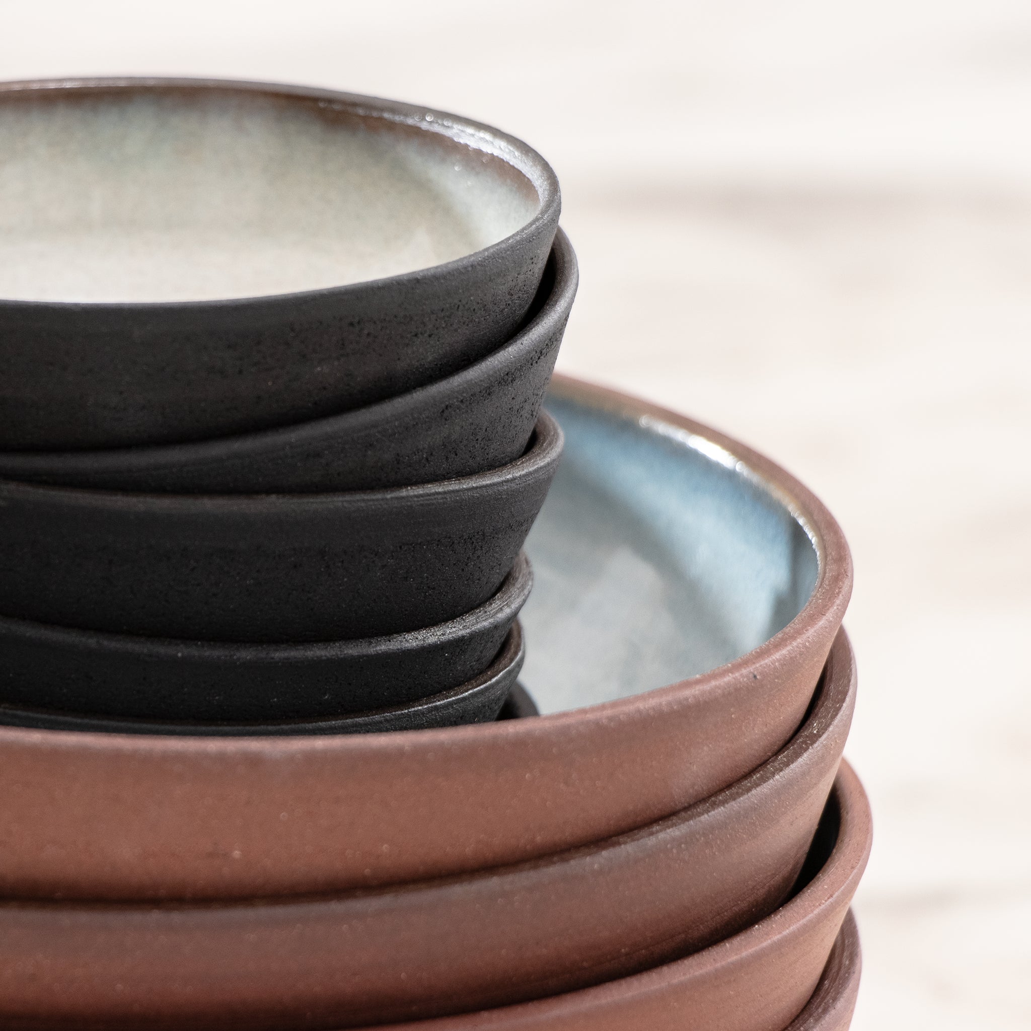 Een close-up van gestapelde Kom Rood Opaal D18 kommen van AB Ceramics laat de gladde, matte afwerking en het minimalistische ontwerp zien. De handgemaakte keramische stukken van AB Ceramics verschijnen op de voorgrond, met een zacht vervaagde achtergrond voor een sereen effect.