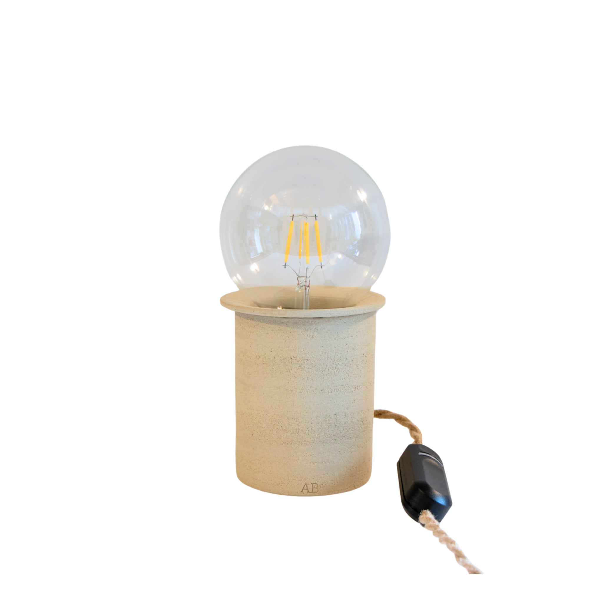 De AB Ceramics LED Lamp Dimmer heeft een ronde, heldere lamp in een eenvoudige beige keramiek voet, een met stof bekleed snoer en een zwarte inline schakelaar. Handgemaakt door AB Ceramics, combineert deze minimalistische lamp stijl en functie.