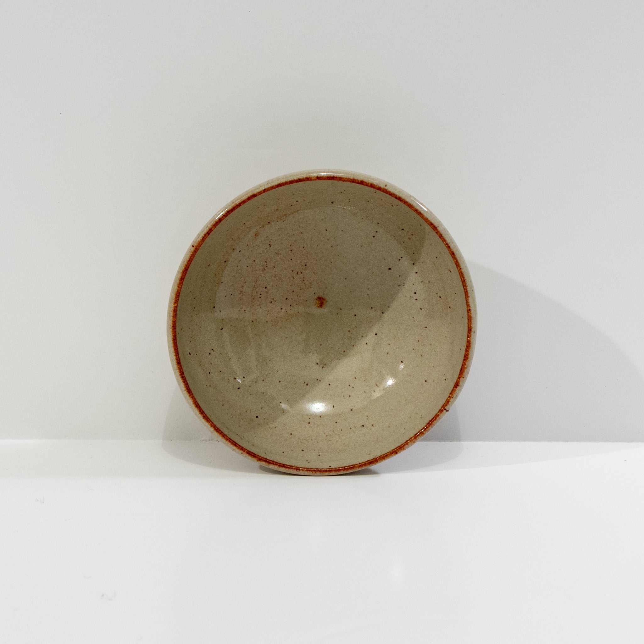 De AB Ceramics Mini Kom Geel Beige D10,5 is een eenvoudige ronde kom van beige steengoed met een roodbruine rand, van boven afgebeeld op een effen witte achtergrond.