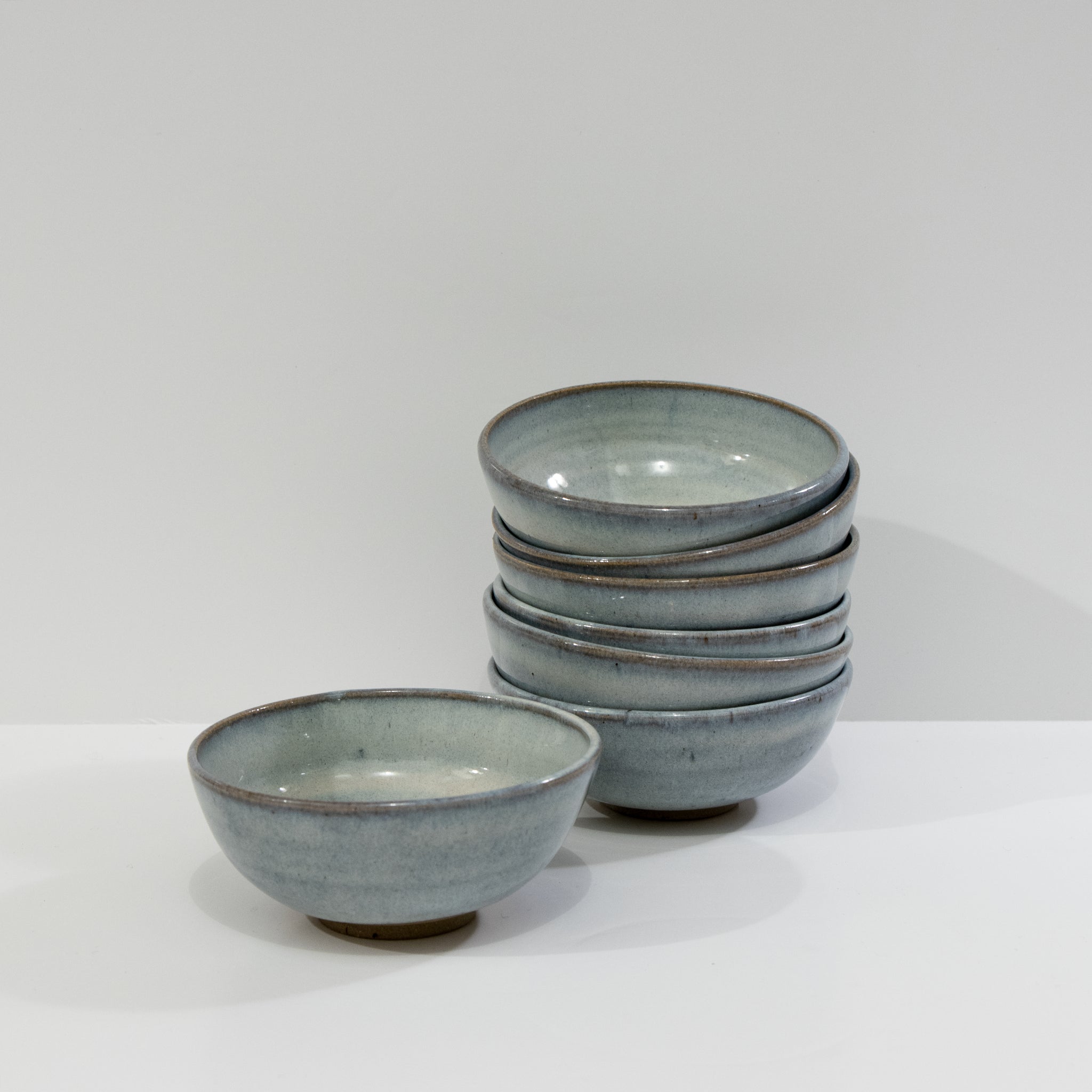 Zes AB Ceramics Mini Kom Geel Opaal D10,5 kommen zijn rechts gestapeld, met één bijpassende kom apart links, tegen een effen witte achtergrond.