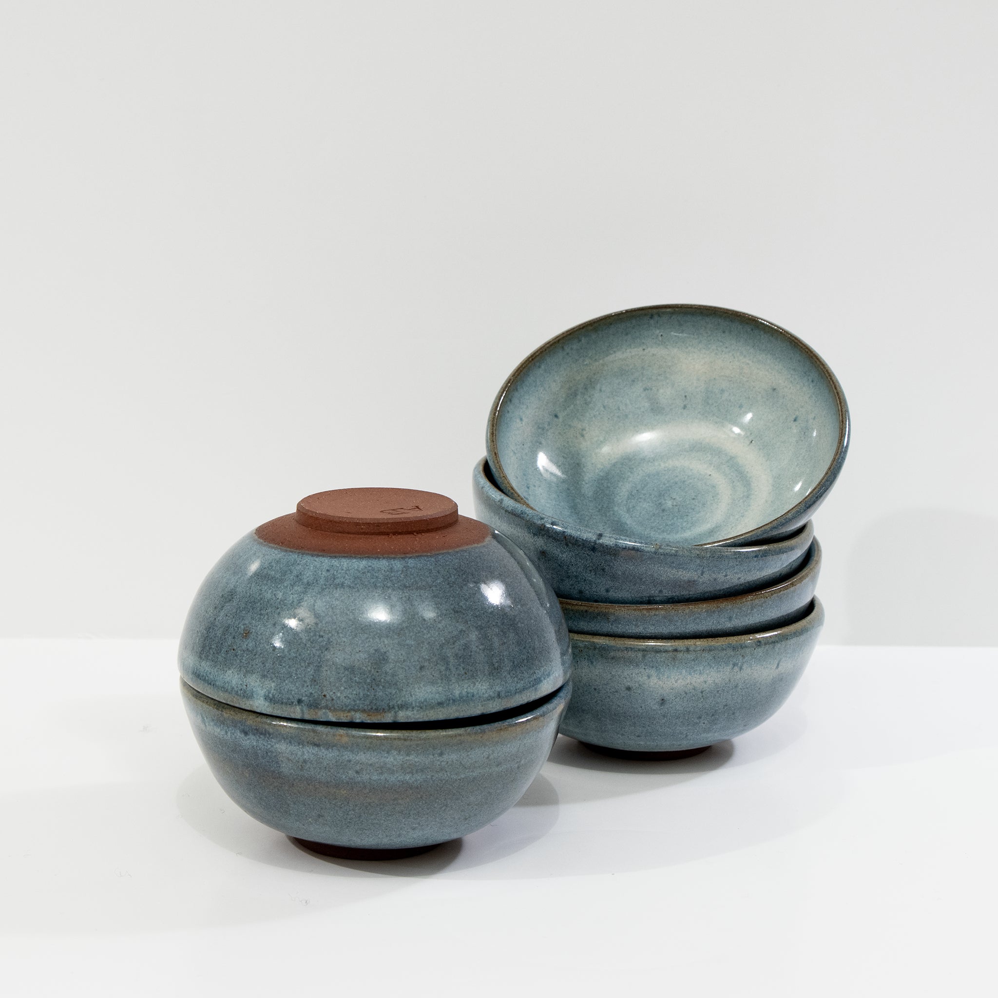 Vijf AB Ceramics Mini Kom Rood Opaal D10,5 schaaltjes worden getoond: vier rechtop gestapeld met een bovenop, de vijfde ondersteboven, waarbij de ongeglazuurde basis zichtbaar wordt. Ze staan allemaal tegen een effen witte achtergrond. Merk: AB Ceramics.