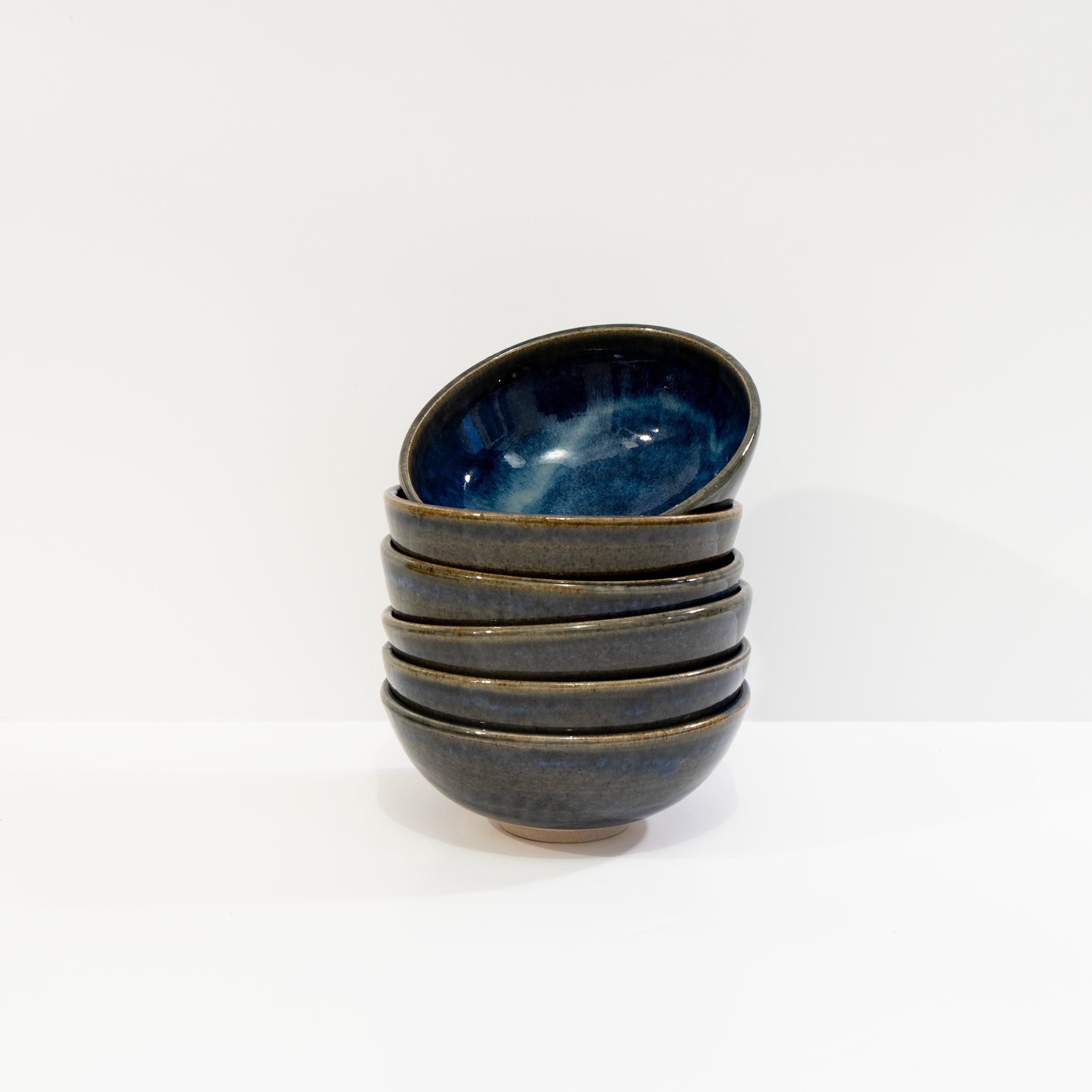 Een stapeltje van zes AB Ceramics Mini Kom Wit Blauwbruin D10,5 schaaltjes, waarvan het bovenste handgedraaide schaaltje iets gekanteld is, tegen een effen witte achtergrond.