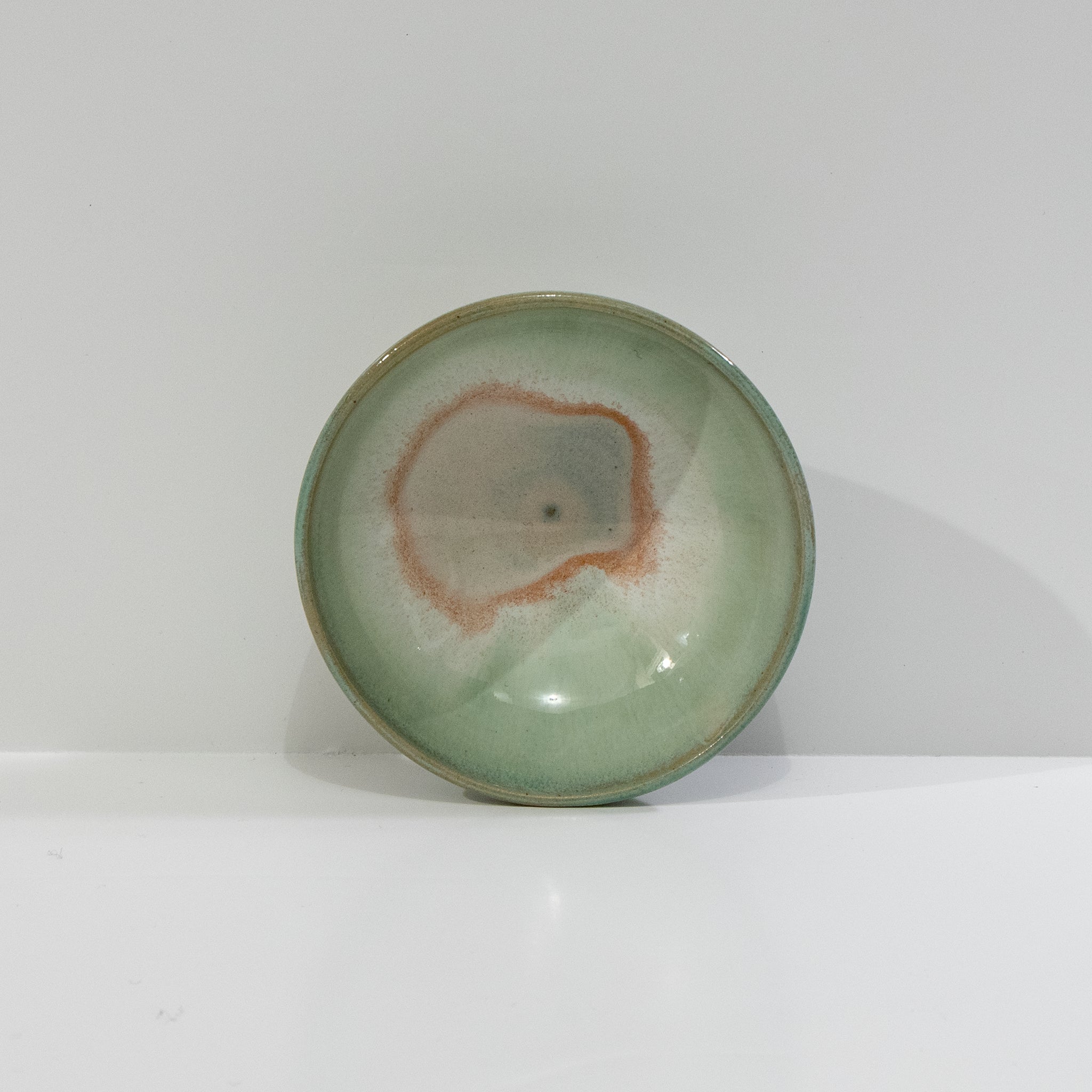 De AB Ceramics Mini Kom Wit Opaal/Lichtgroen D10,5 is een ronde steengoed schaal met een glanzend lichtgroen glazuur en centrale roodbruine details, met subtiele kleurvariatie, afgebeeld op een effen witte achtergrond.