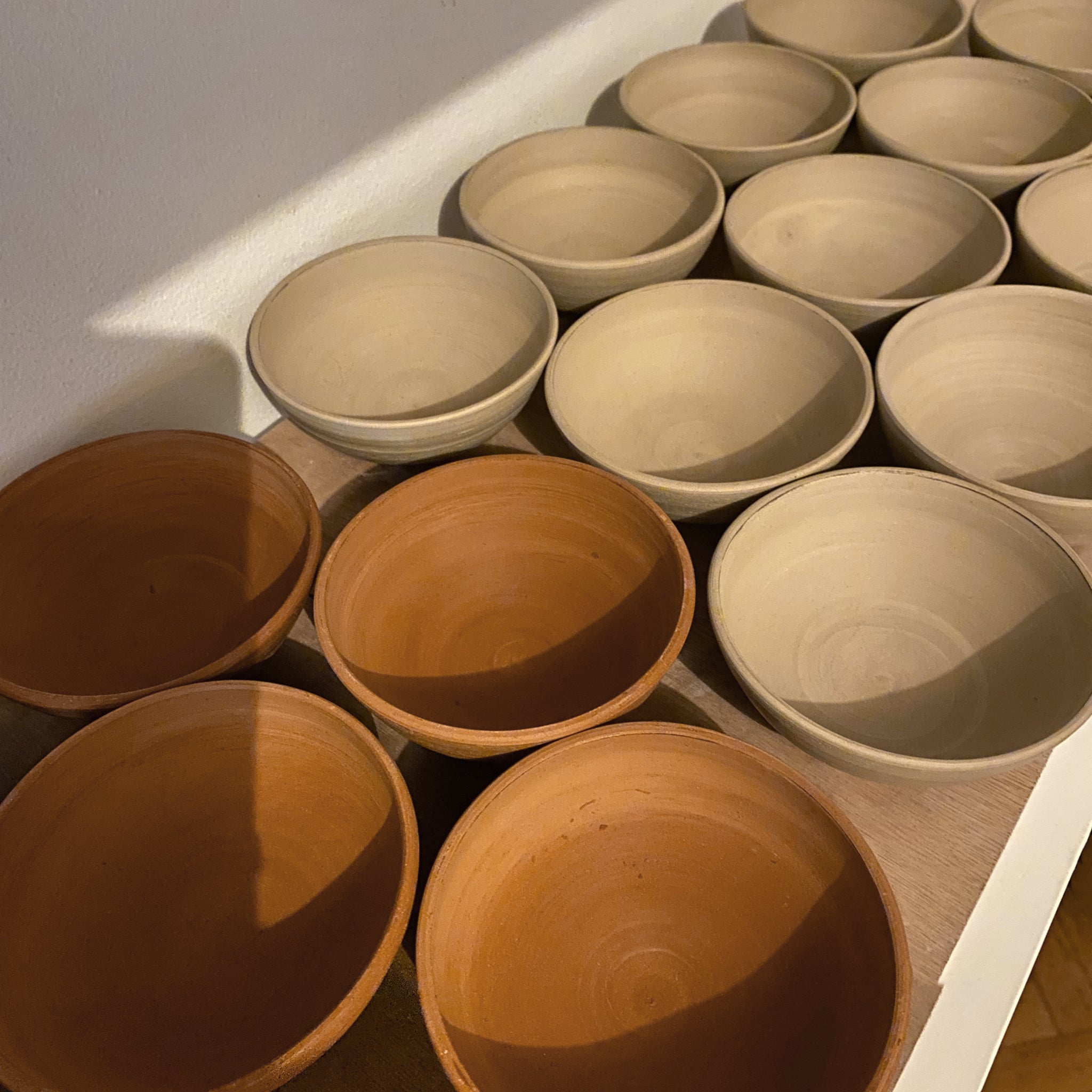 De Mini Kom Wit Opaal/Lichtgroen D10,5 kommen van AB Ceramics, vakkundig vervaardigd van steengoed keramiek, staan op een houten ondergrond; hun lichte glazuur en unieke handgemaakte afwerking schitteren onder zacht binnenlicht.