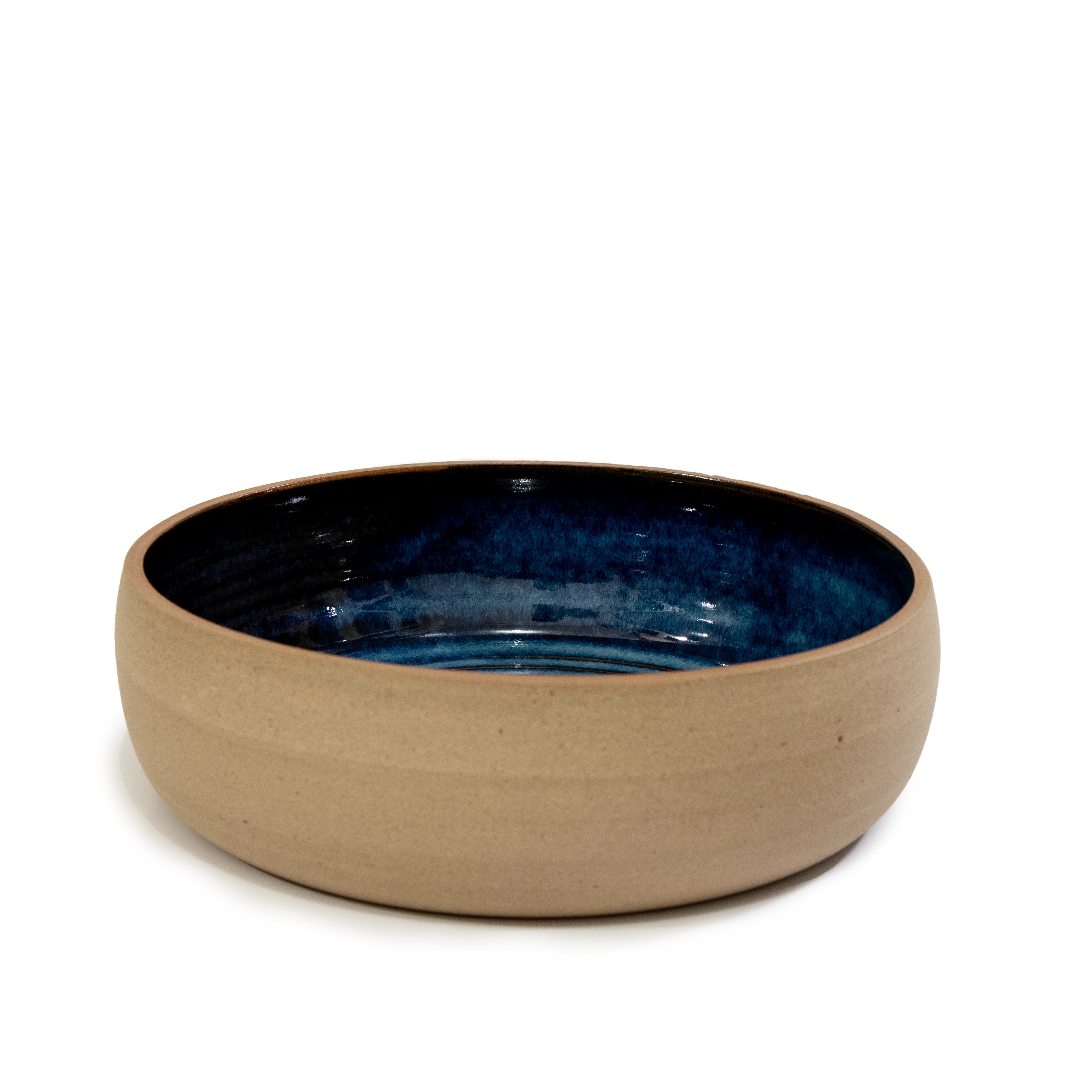 De AB Ceramics Serveerschaal Spiraal Geel Blauw D21,5 Laag is een handgemaakte keramische schaal met mat beige buitenkant en glanzend donkerblauw interieur, uniek servies van AB Ceramics op een witte achtergrond.