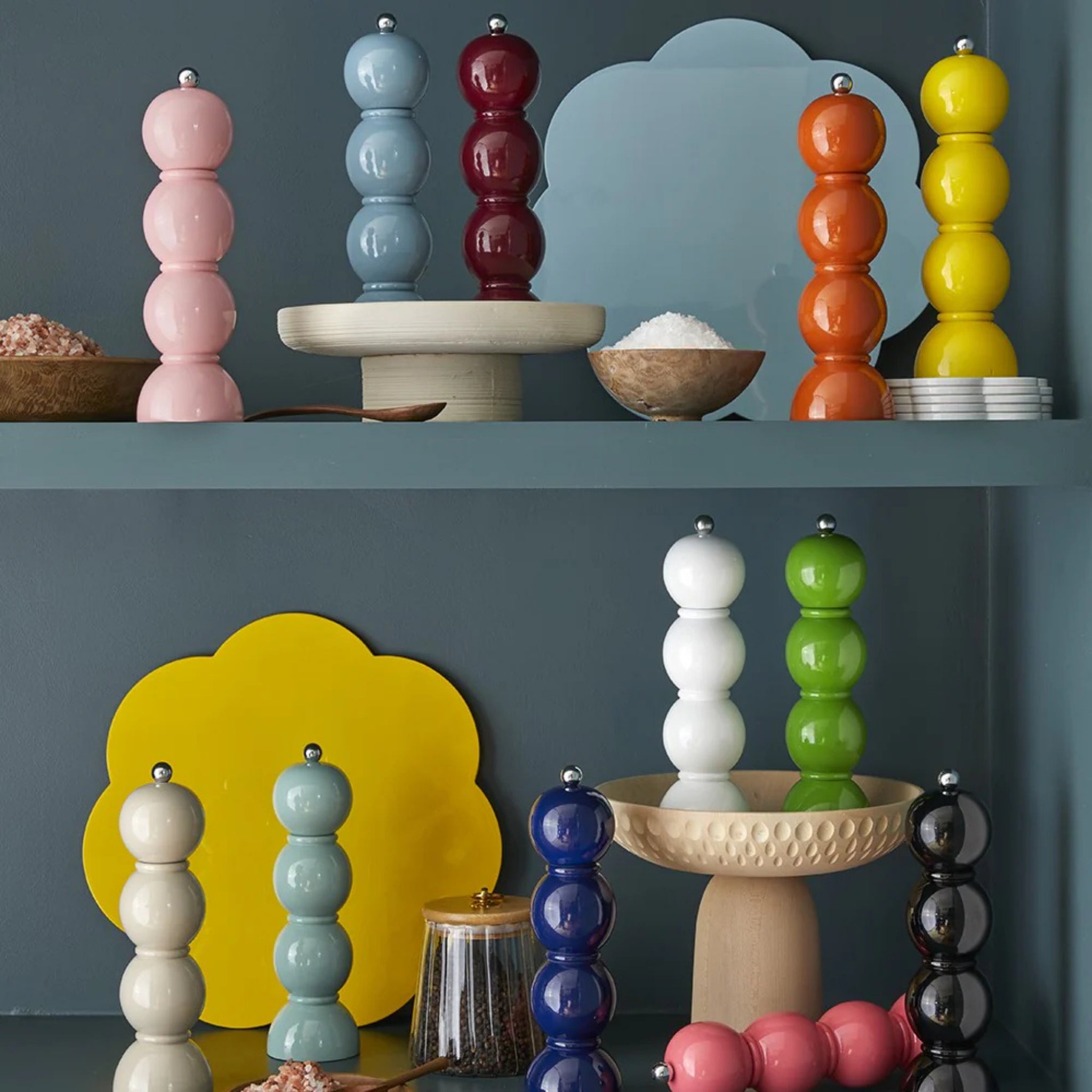 De Addison Ross Bobbin Zout-en Pepermolen Racing Groen 24 cm staat mooi op blauwe planken, omringd door zoutkommen, kleine bordjes en gele en lichtblauwe wolkvormige borden voor een levendige, moderne keukenlook.