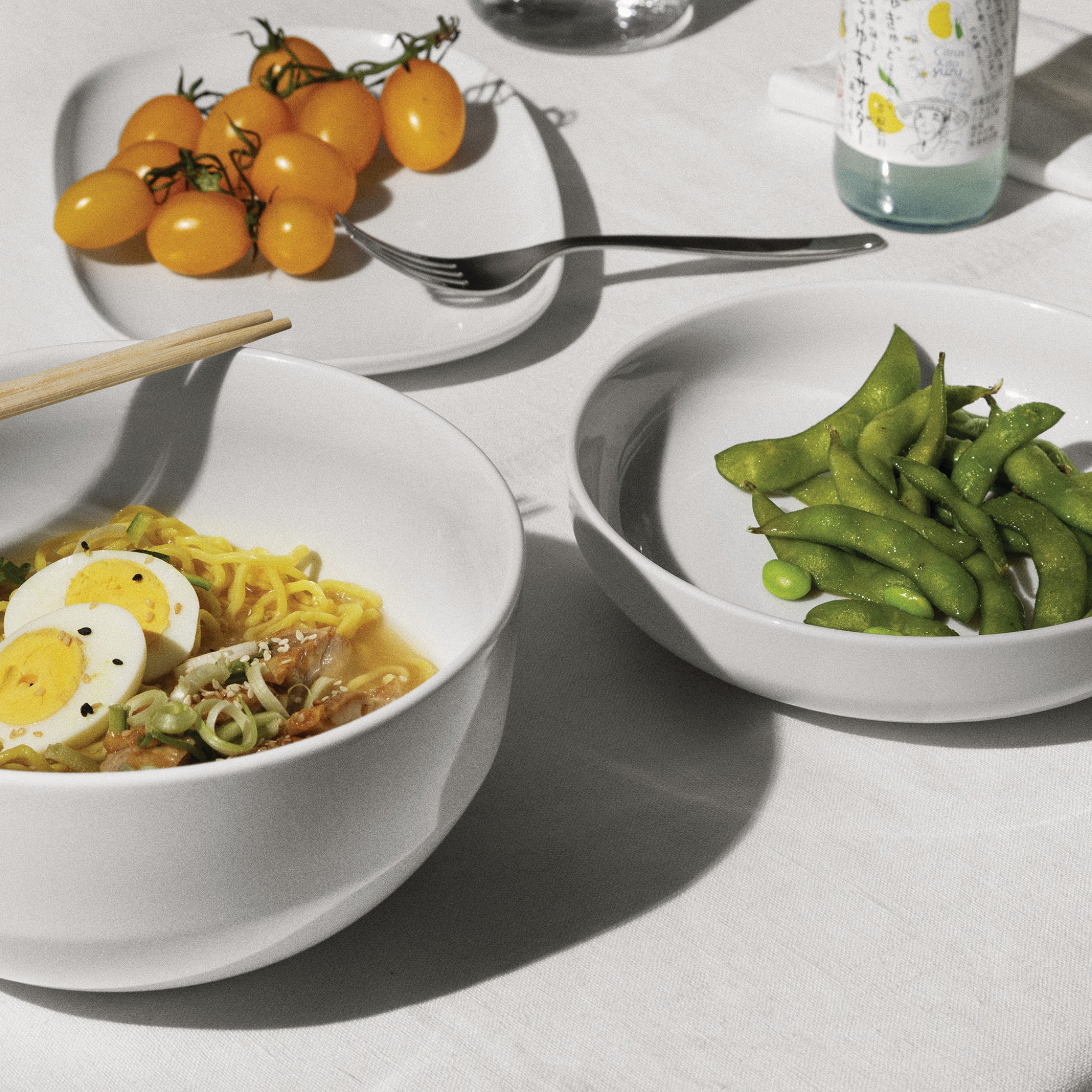 Een kom ramen met ei, edamame en gele tomaten wordt geserveerd in de Alessi Itsumo Saladekom Wit 195 cl, een stuk van Alessi dat Japans geïnspireerd design en verfijnde elegantie weerspiegelt.