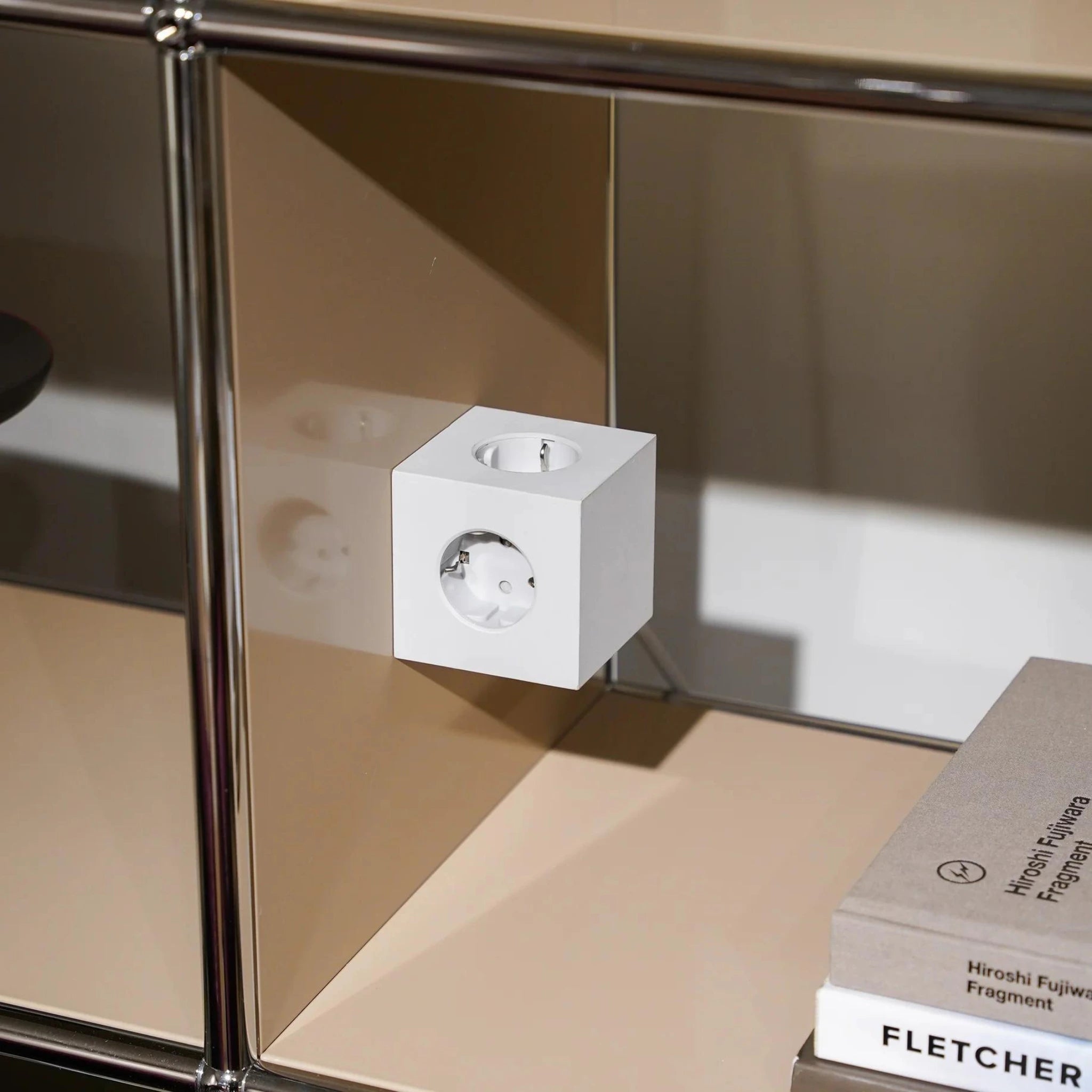 Een Avolt Square 1 USB-C Stekkerdoos Gotland Grijs 1,8 m van Avolt is gemonteerd op een beige en metalen schap, met netjes gestapelde boeken in de buurt voor een moderne, minimalistische look.