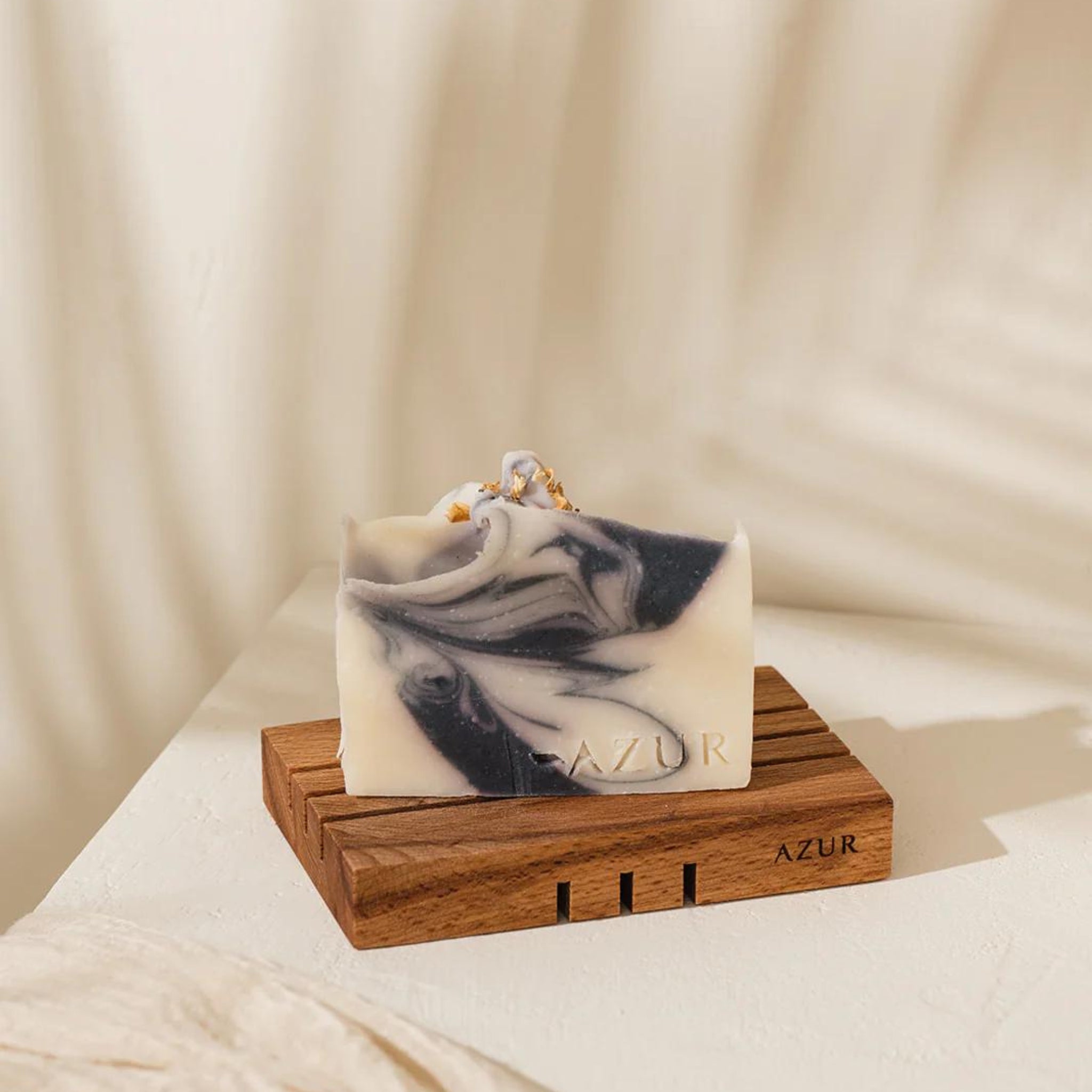 Een ambachtelijke rechthoekige zeepstaaf met zwarte en witte krullen zit op de Azur Houten Zeephouder, een houten zeephouder van Azur, tegen een zachte neutrale achtergrond voor een minimale en elegante uitstraling.
