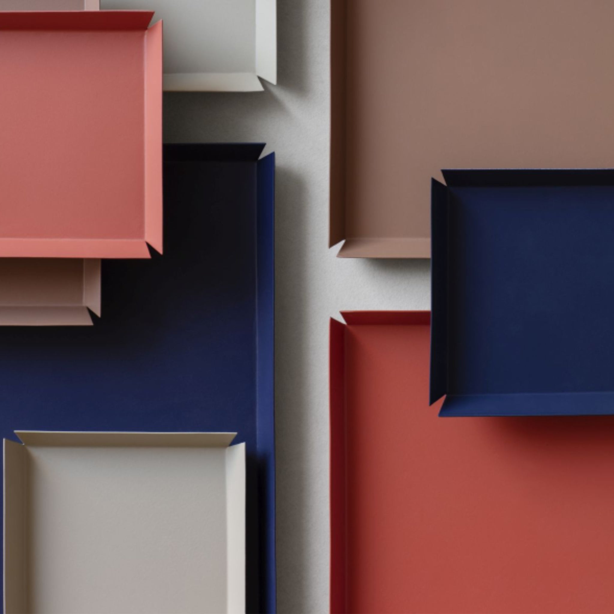 Het Broste Copenhagen Erika Dienblad Zand 43/33 van Broste Copenhagen heeft een geometrisch, overlappend patroon met dienbladen in rood, marineblauw, beige en bruin op een lichtgrijs oppervlak. Perfect als multifunctioneel dienblad.