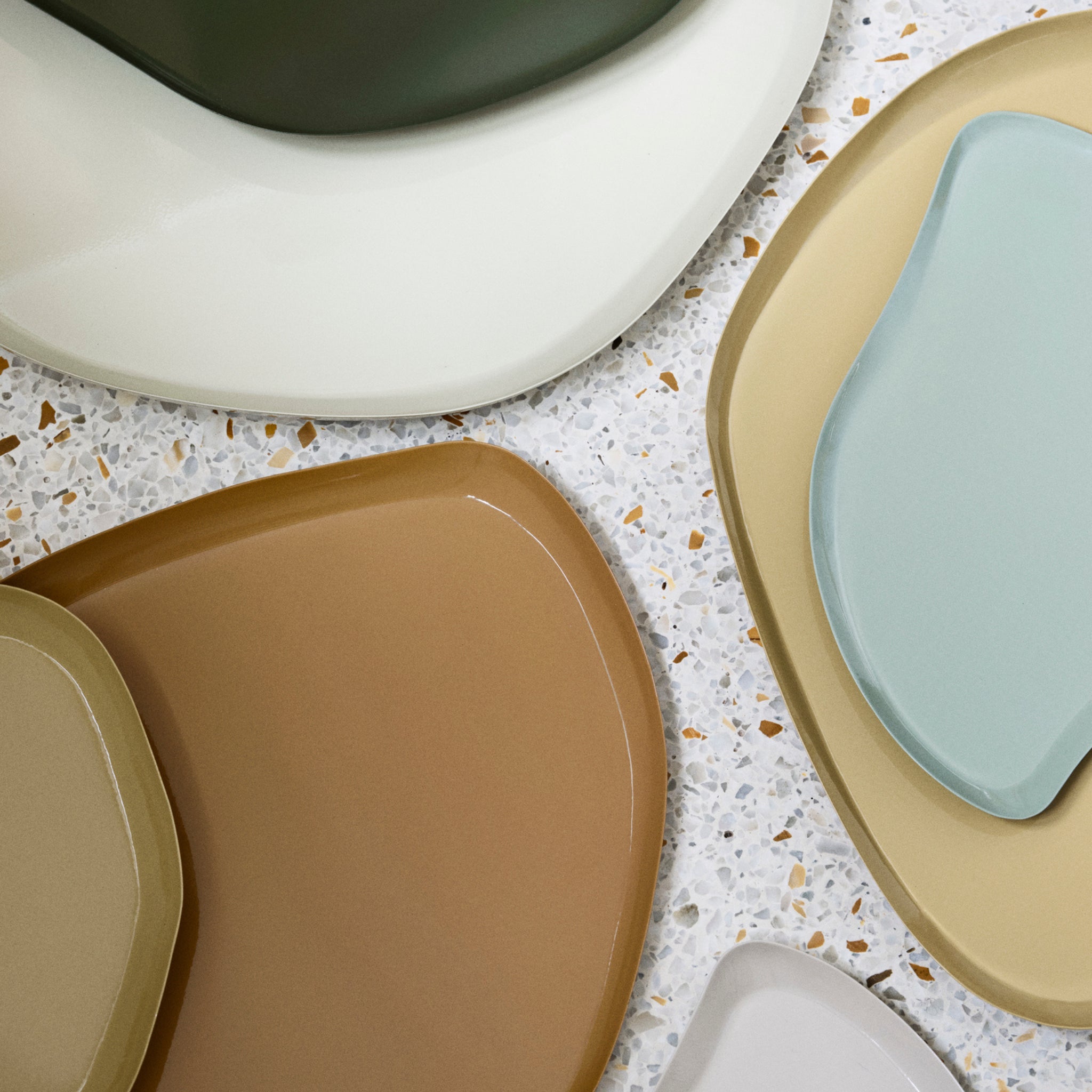 Een close-up van het Broste Copenhagen Mie Dienblad L Taupe Zand 39/32, een modern, onregelmatig gevormd dienblad in neutrale tinten, gerangschikt op een gespikkeld oppervlak.