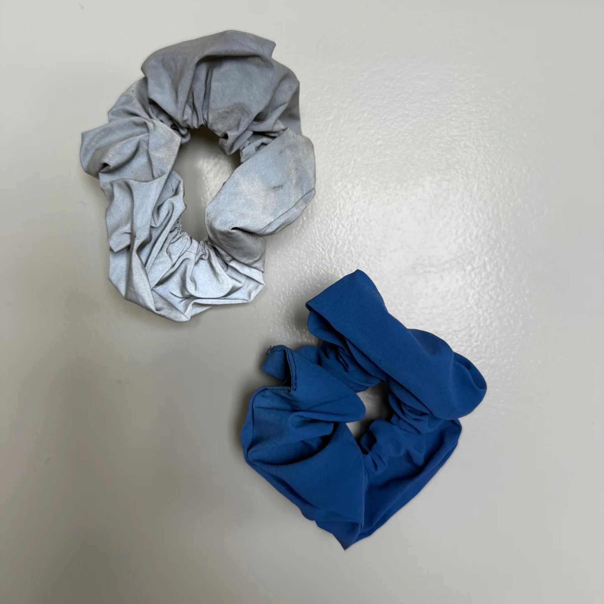 De Caro Antwerp Caro The Scrunch Club Scrunchie 2 st. set bestaat uit twee grote scrunchies, een lichtgrijze en een blauwe, ideaal voor extra zichtbaarheid of als een unieke fiets accessoire.
