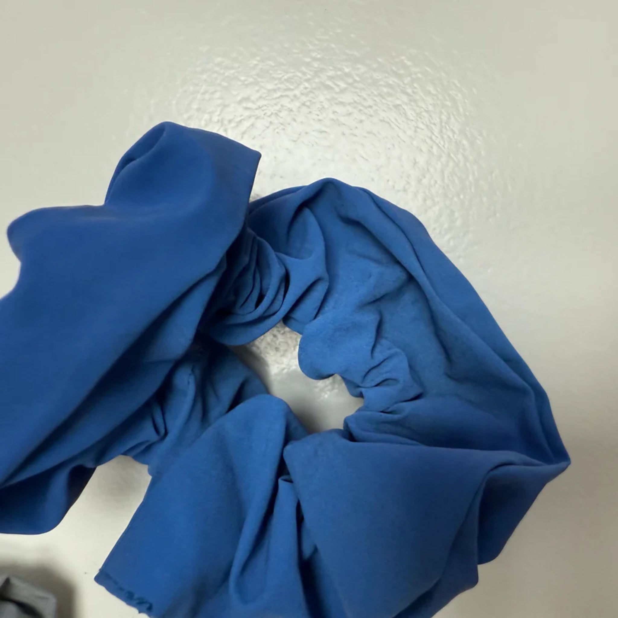Een Caro Antwerp Caro The Scrunch Club Scrunchie 2 st. in blauw met een reflecterende afwerking rust op een licht oppervlak, de zachte plooien vormen een ongelijke cirkel-ideaal als een trendy fiets accessoire voor extra zichtbaarheid.