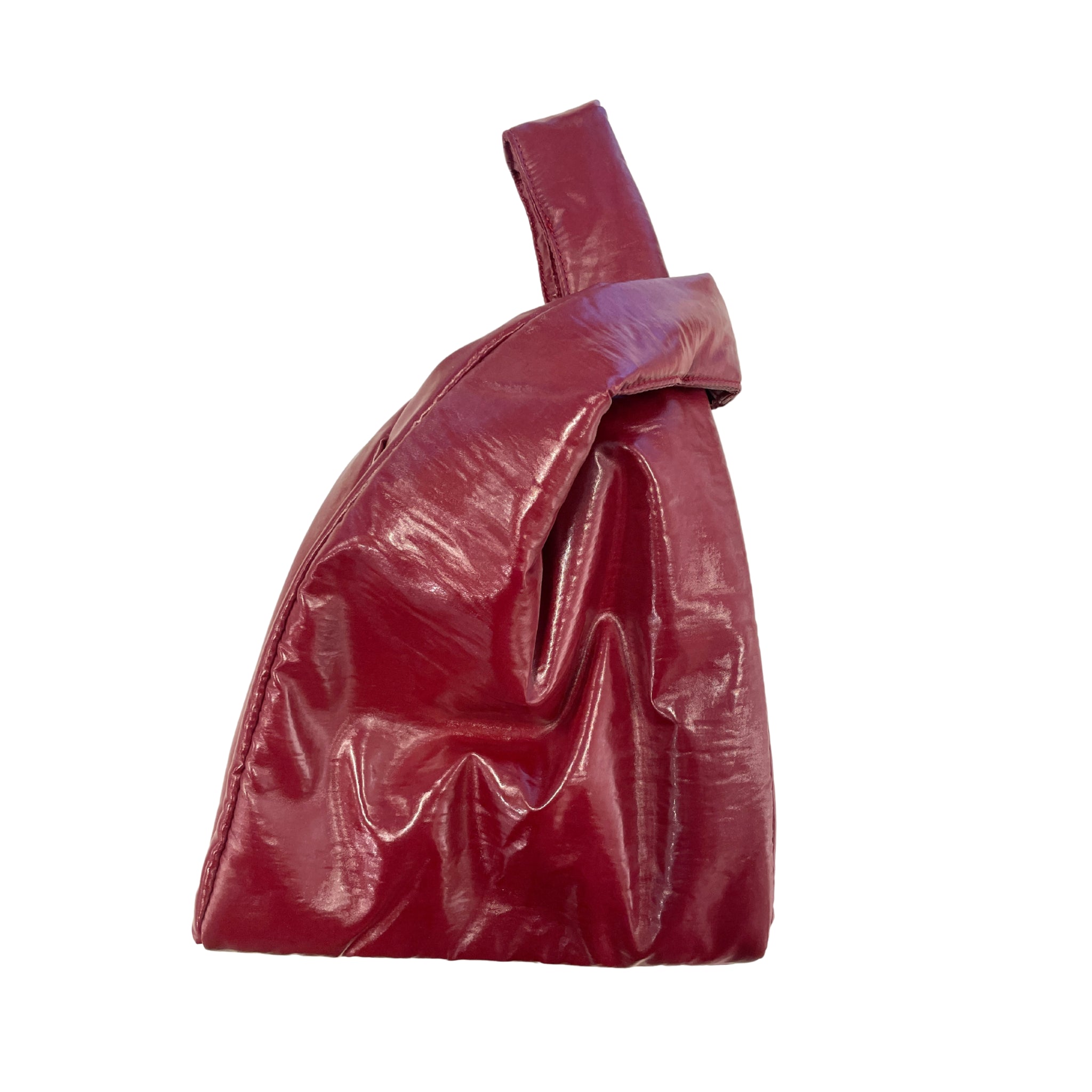 De Caro Handtas Chubby Barolo Bordeaux van Caro Antwerp, een glanzend rode pofzak met enkele riem en gedraaid bovenhandvat, staat rechtop tegen een witte achtergrond-een opvallende verschijning uit hun handtassencollectie.