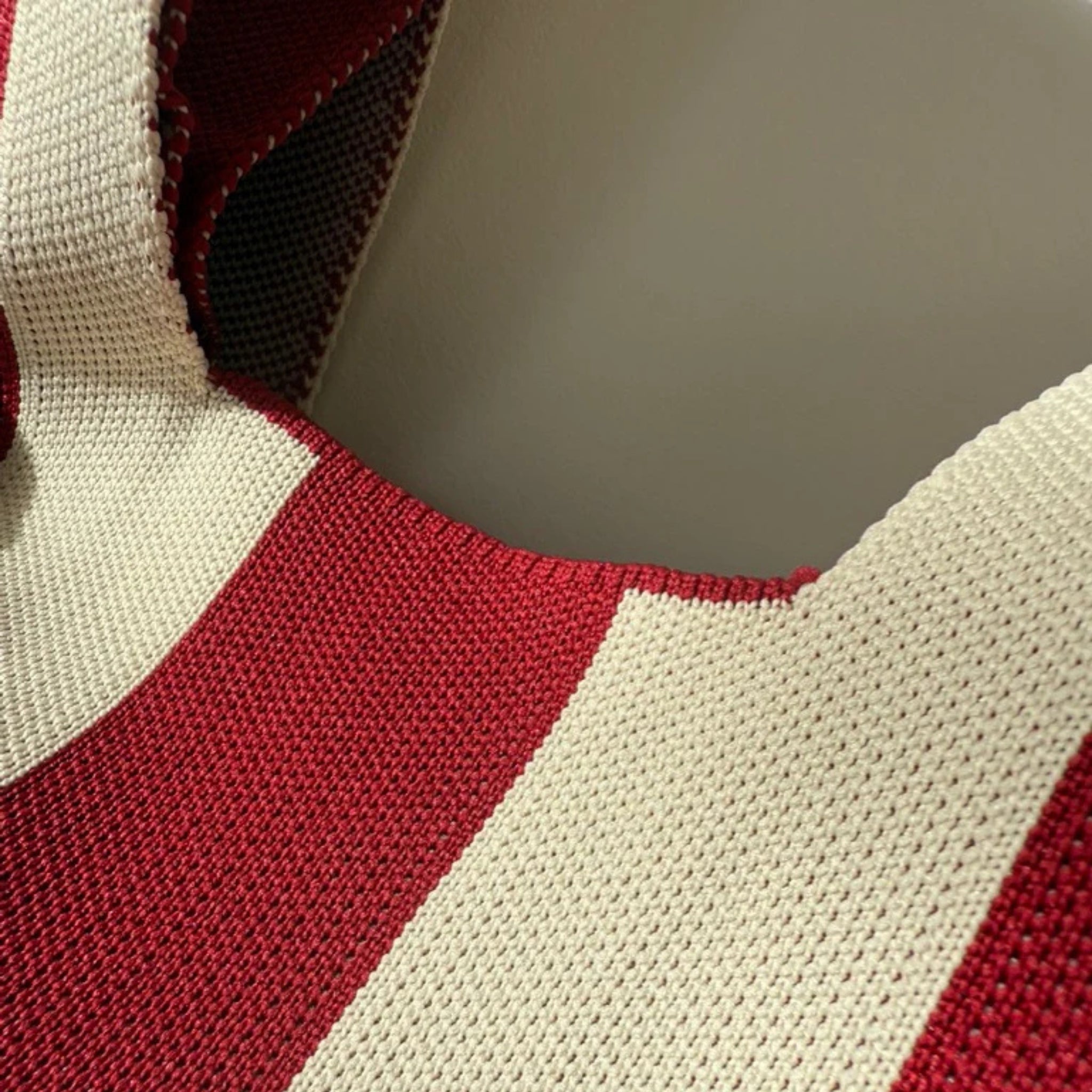Close-up van rode en beige strepen op een gebreide stof uit de Caro Handtas Stripe The Casual van Caro Antwerp, tegen een gladde grijze achtergrond. De textuur en stikseldetails zijn duidelijk zichtbaar.