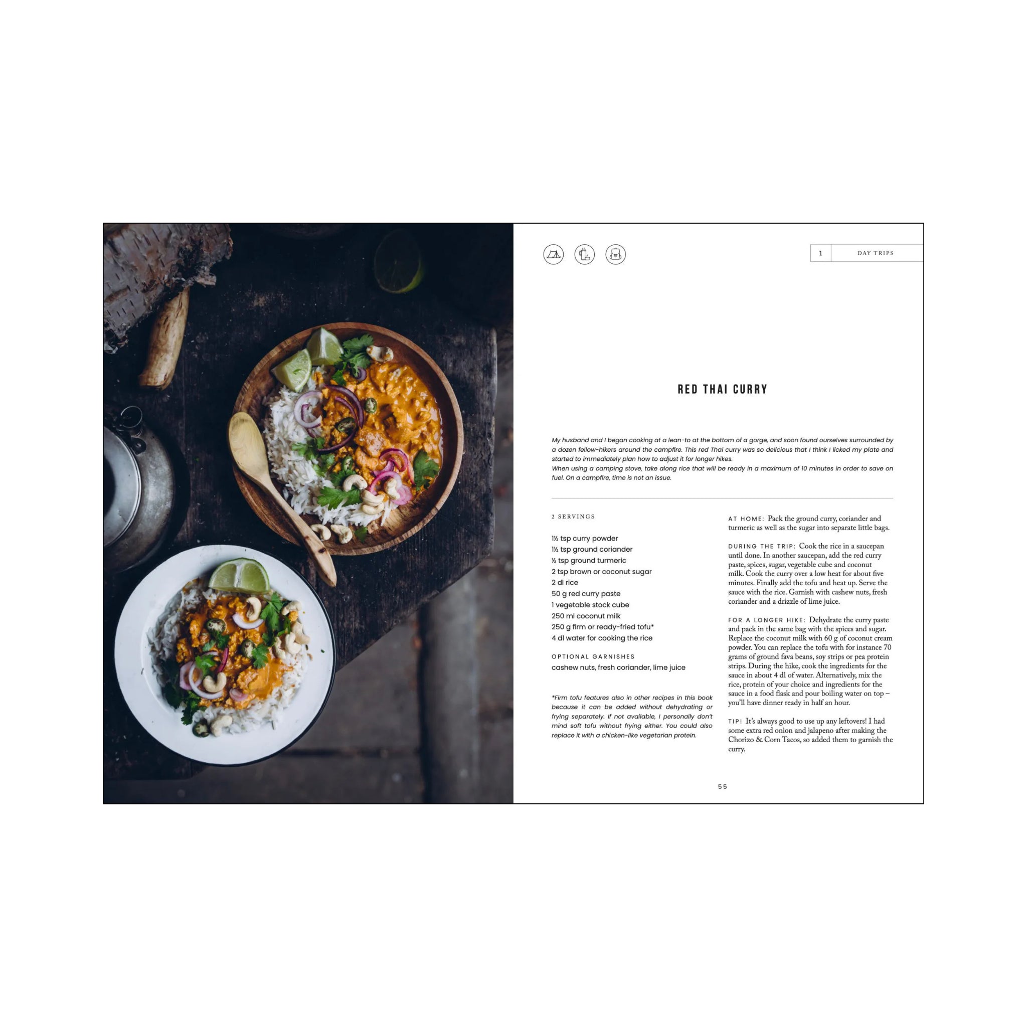 Het Kookboek Food in the Woods van Cozy Publishing staat open voor een recept voor Red Thai Curry, ideaal voor vegetarische recepten, naast twee kommen met levendige curry en rijst gegarneerd met kruiden, uien en limoen op een rustieke houten tafel.
