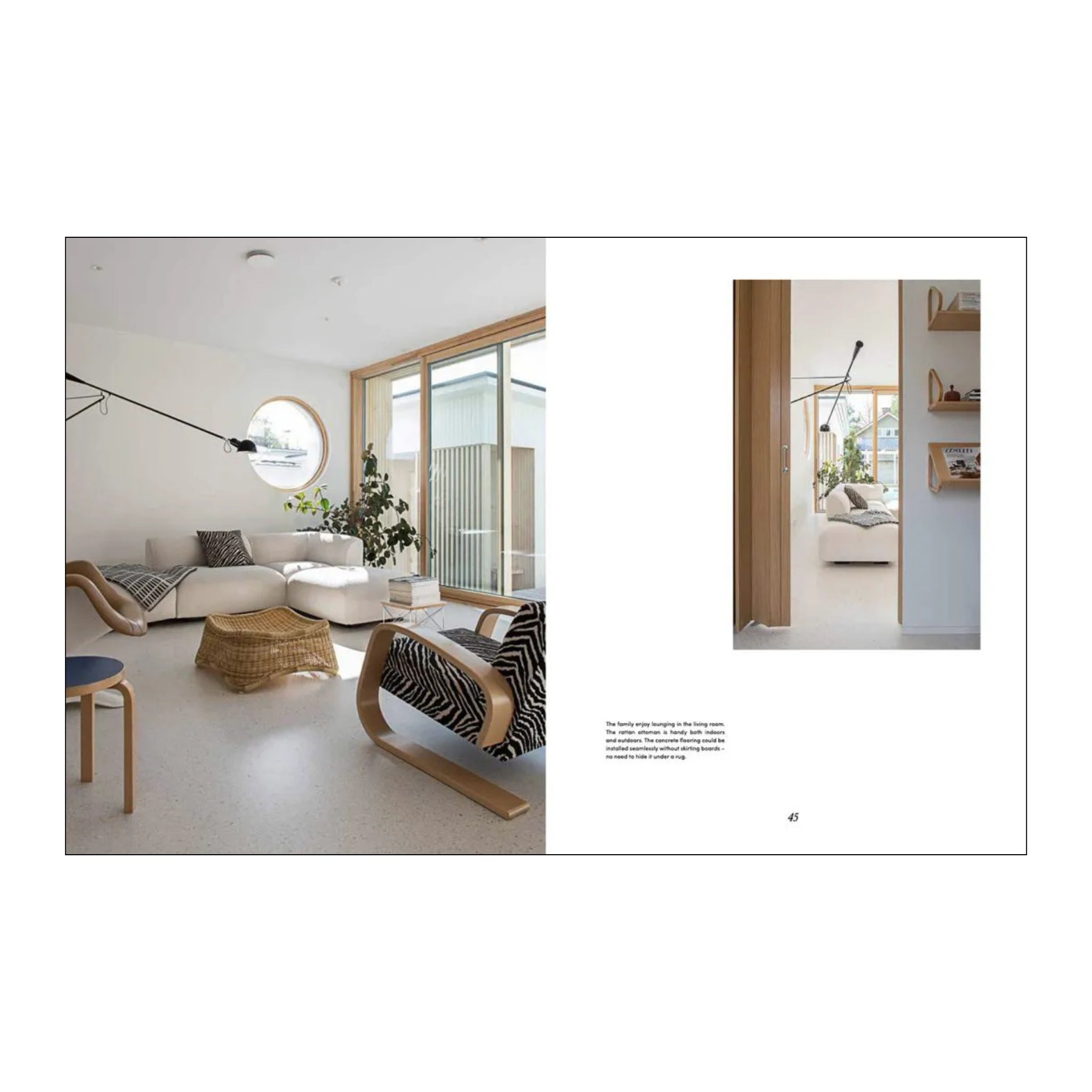 Een lichte, moderne woonkamer met natuurlijk licht, neutrale meubels, een geweven salontafel en Scandinavische stijl. Grote ramen en gedessineerde kussens voegen charme toe; in de inzet staan planken in de hal met het Soft Nordic Boek van Cozy Publishing.