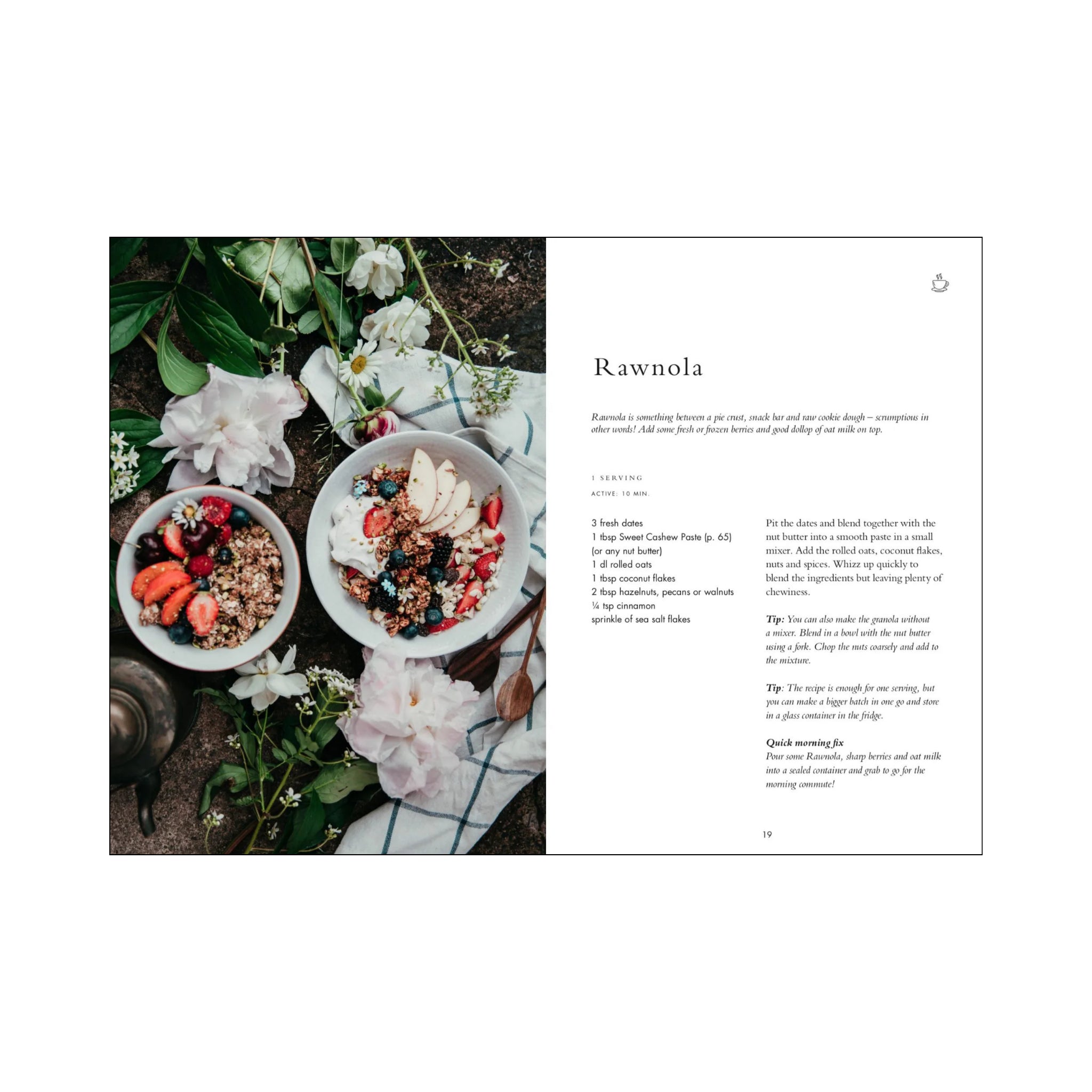 Twee schaaltjes met rauwe granola en fruit rusten op een rustieke ondergrond met bloemen en groen. Het Cozy Publishing Wonderful Morning Kookboek van Cozy Publishing, met rawnola ontbijt recepten, wordt rechts getoond.
