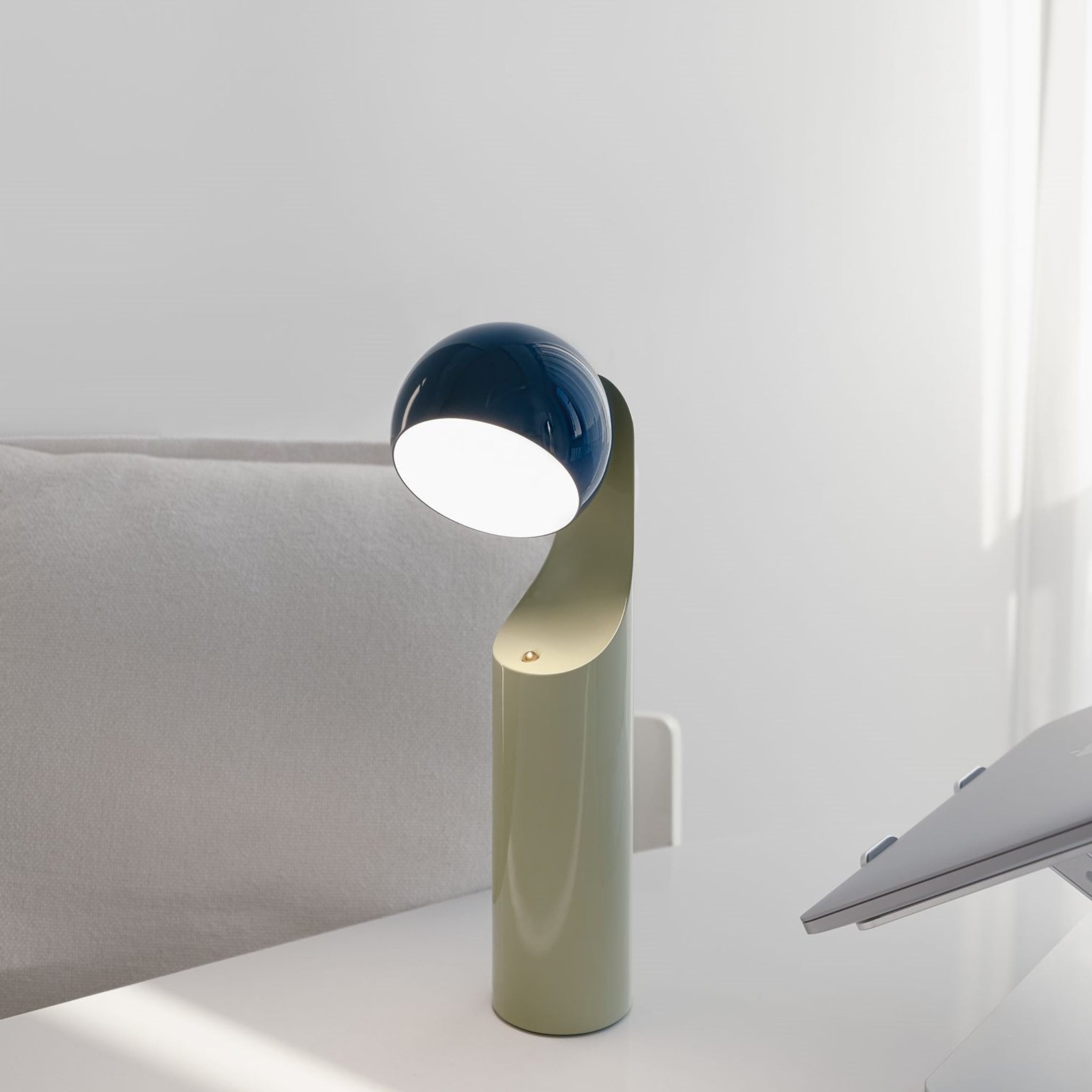 De Fine Lumens Mono Leeslamp LED Oplaadbaar Blauw Munt heeft een gebogen lichtgroene basis en donkerblauwe koepelkop, die instelbaar LED-licht op je bureau werpt en elegantie en functionaliteit toevoegt aan elke werkruimte.