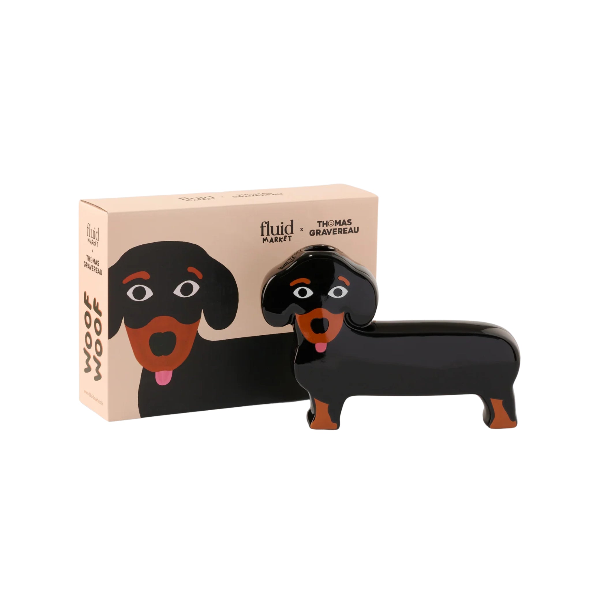 De Fluid Market Teckel Vaas is een keramisch teckelfiguurtje in zwart en bruin met een roze tong en vriendelijke uitdrukking, voor zijn doos met afbeeldingen van een hond en "fluid" plus "WOOF WOOF." Een uniek woonaccessoire van Fluid Market.