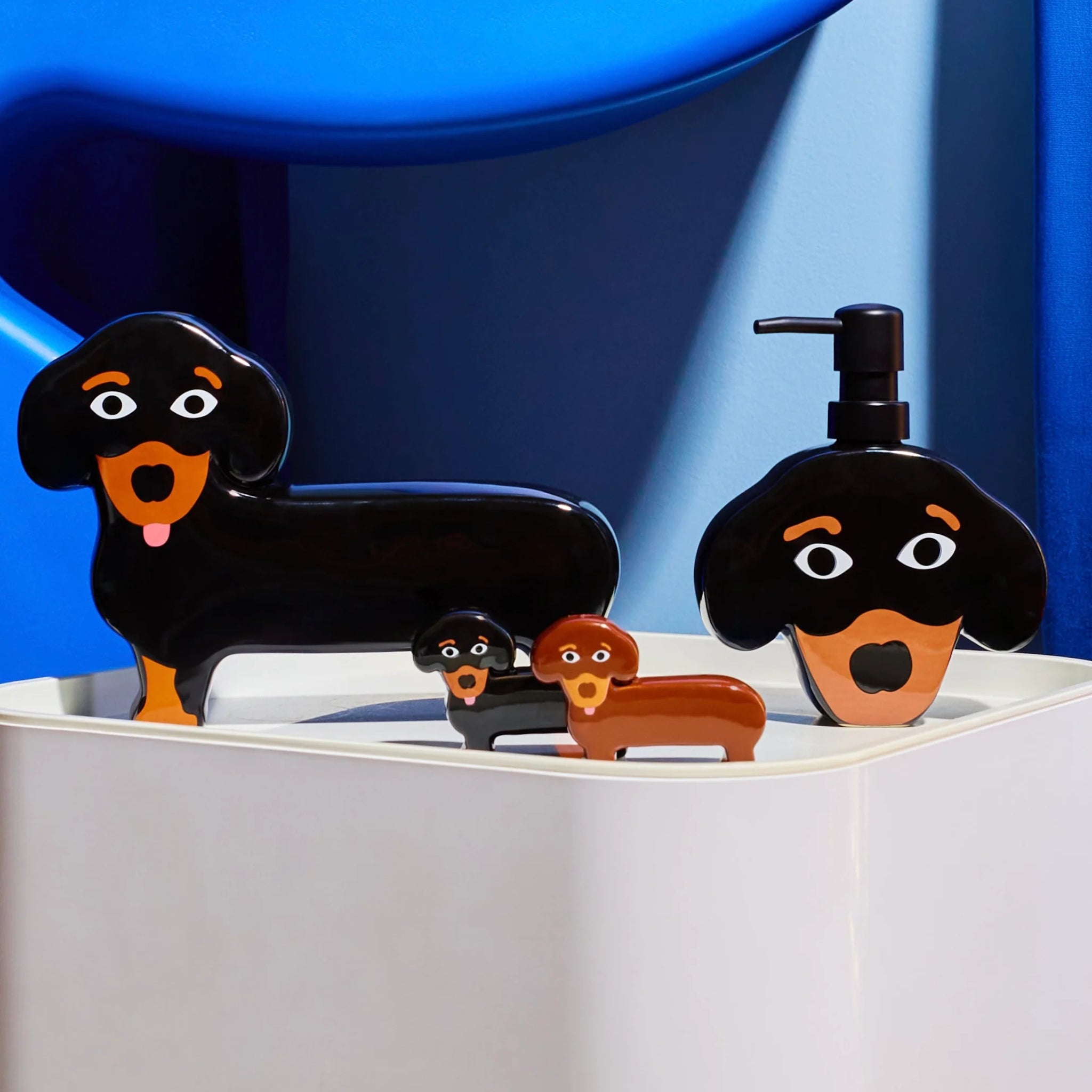 De Fluid Market Zout- en Pepervaatjes Teckel 2 st. -zwarte en bruine teckels van keramiek met cartoongezichtjes- worden weergegeven op een wit oppervlak tegen een blauwe achtergrond, wat zorgt voor een speels en leuk cadeau.