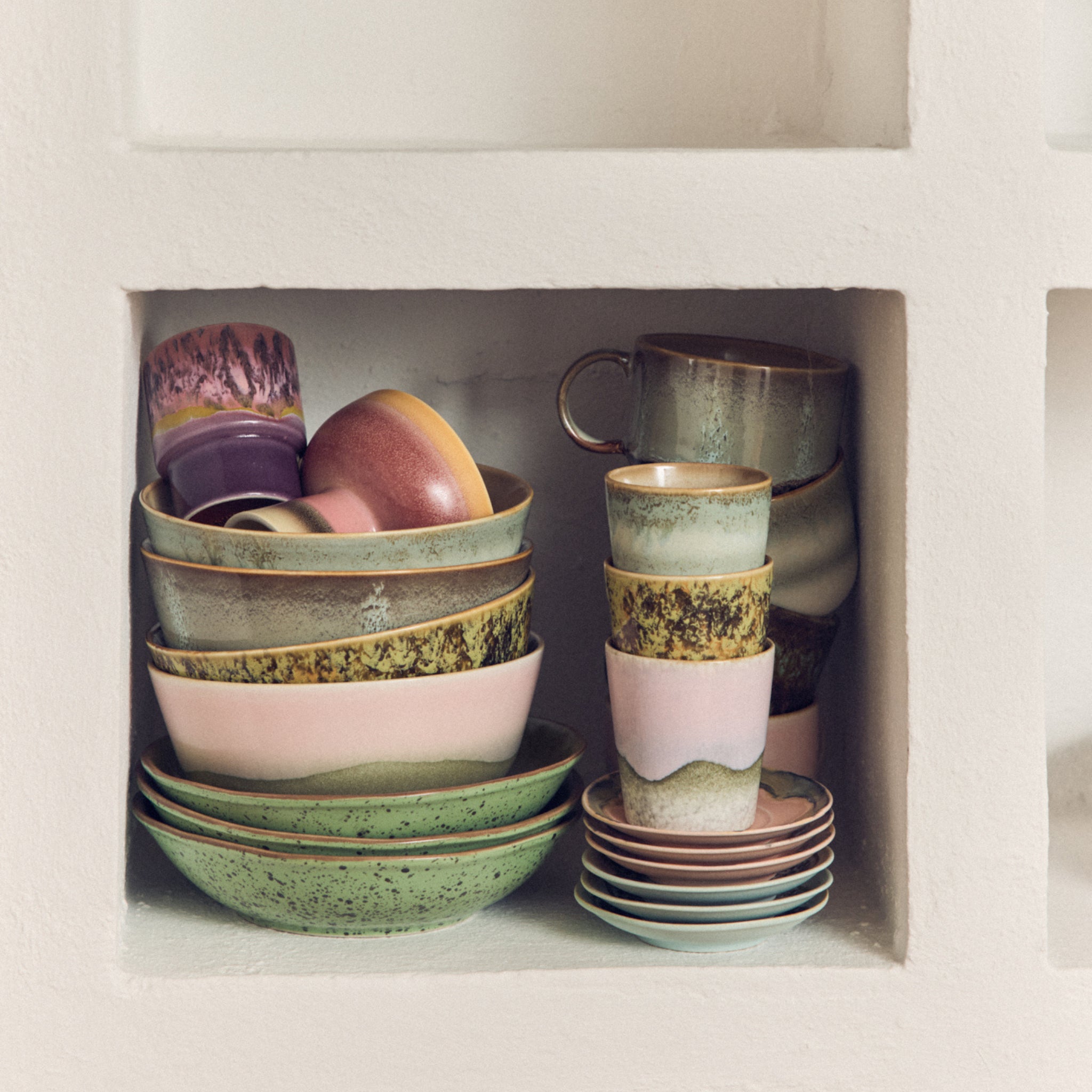 De HK Living 70s Ceramics Koffiekop Bramble toont pastelkleurige en aardse tinten met handgemaakt structuurglazuur, netjes gestapeld op een witte wandplank voor een levendige, ambachtelijke touch.