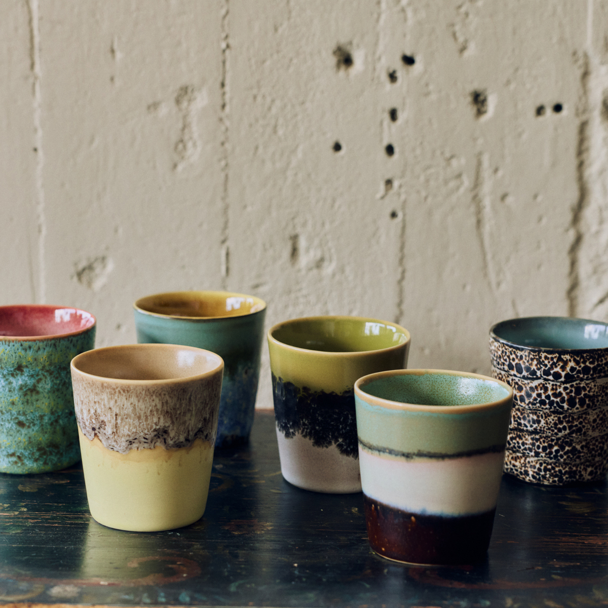 Zes HK Living 70s Ceramics Koffiekoppen op een donkere houten tafel: Zingy, Custard, Agave, Truffle, Gelato en Brew