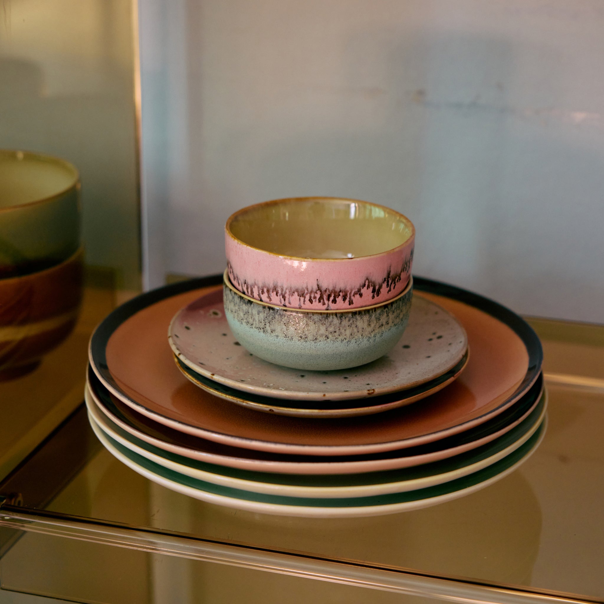 Een stapel HK Living 70s Ceramics borden in aardetinten wordt afgemaakt met twee Renaissance tapasschaaltjes van HK Living - een in roze en goud met een decoratieve rand, de andere groen en gespikkeld.