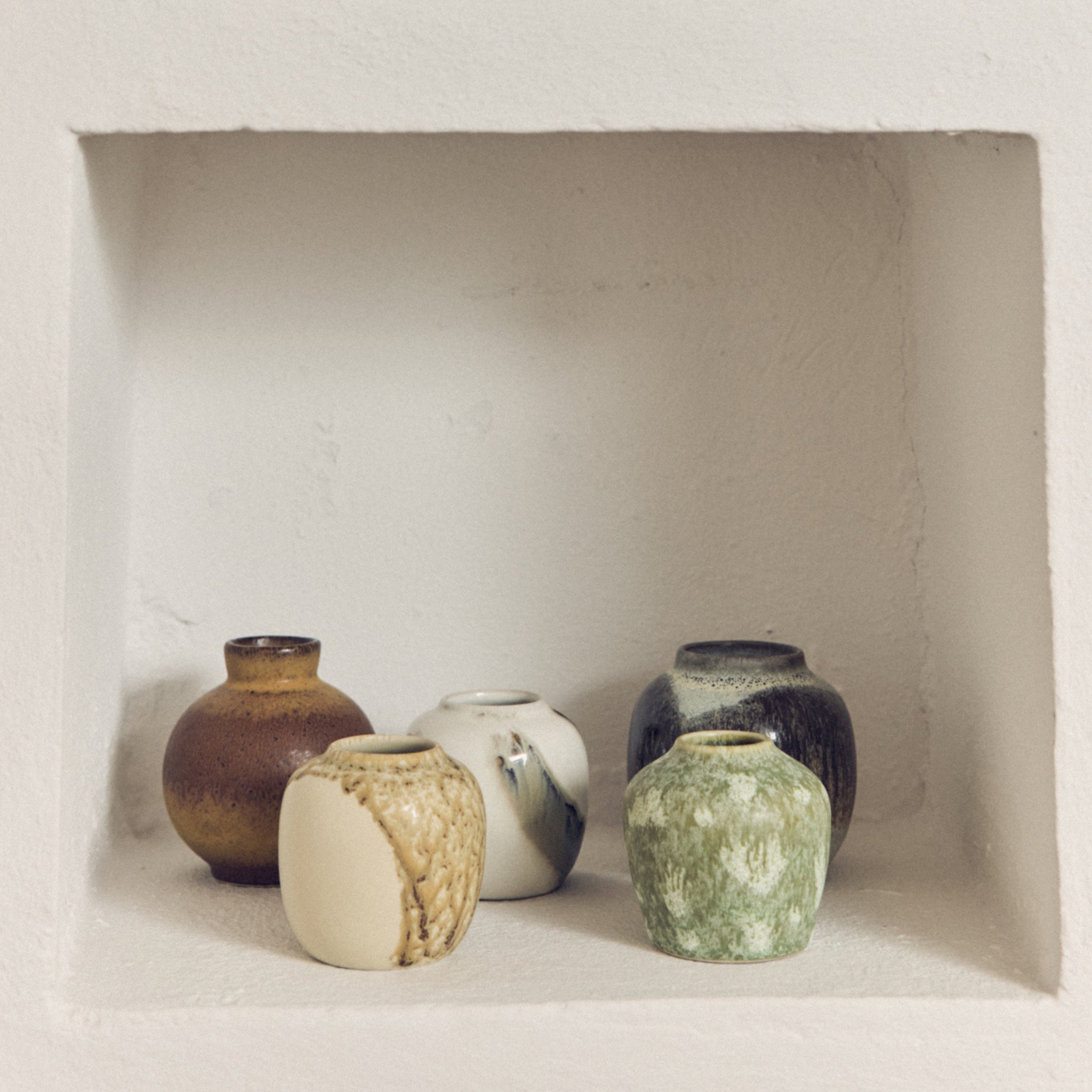 Vijf HK Living 70s Ceramics Vaasjes Pursuit (set van 5) in aardetinten en verschillende texturen staan op een witte, matte nisplank-ideaal voor retro interieurdecoratie.