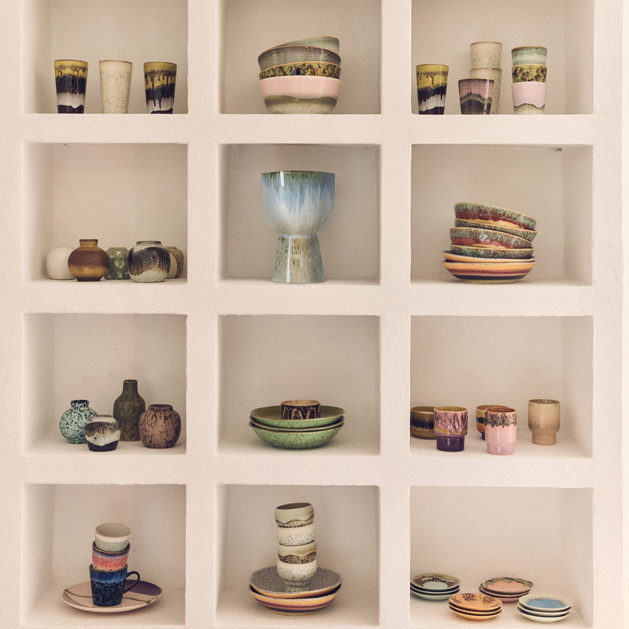 Kleurrijke keramische kommen, kopjes, borden en de HK Living 70s Ceramics Vaasjes Pursuit (5 st.) van HK Living zijn gerangschikt op een witte ingebouwde plank met drie rijen-ideaal voor retro interieur decoratie. Elke nis benadrukt unieke stukken aardewerk.