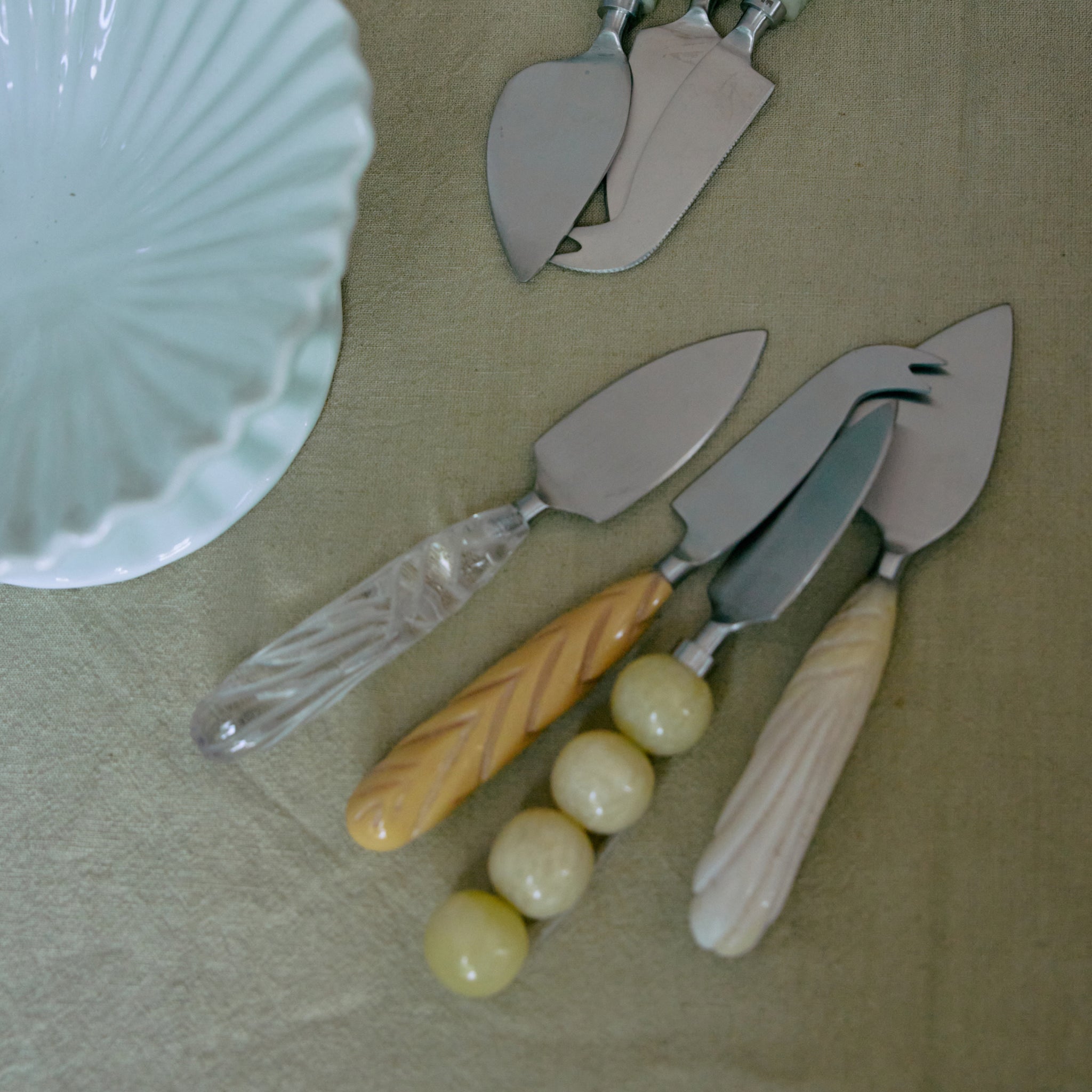 Vier vintage taartscheppen met decoratieve handgrepen rusten op een licht tafelkleed naast een witte keramische schaal met geschulpte rand - een perfecte aanvulling op uw HK Living Kaasmesjes Crème 3 st. set.