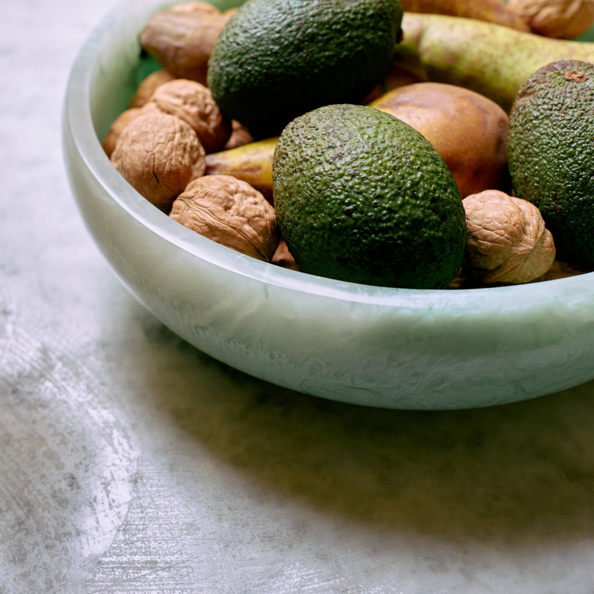 Een HK Living Saladekom Mint D26 van HK Living, gevuld met avocado's, walnoten en peren, staat op een grijs gestructureerd oppervlak.
