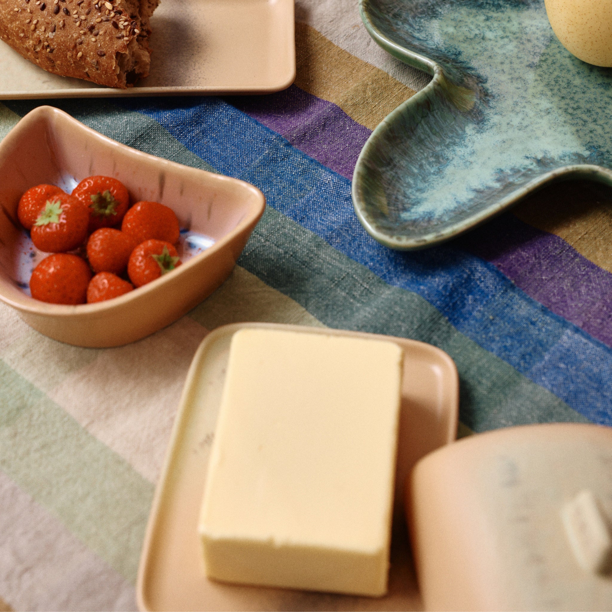 Een gestreept tafelkleed houdt een bord aardbeien, volkoren brood en boter geserveerd in de HK Living 70s Ceramics Botervlootje Breeze van HK Living op een groen keramisch dienblad.