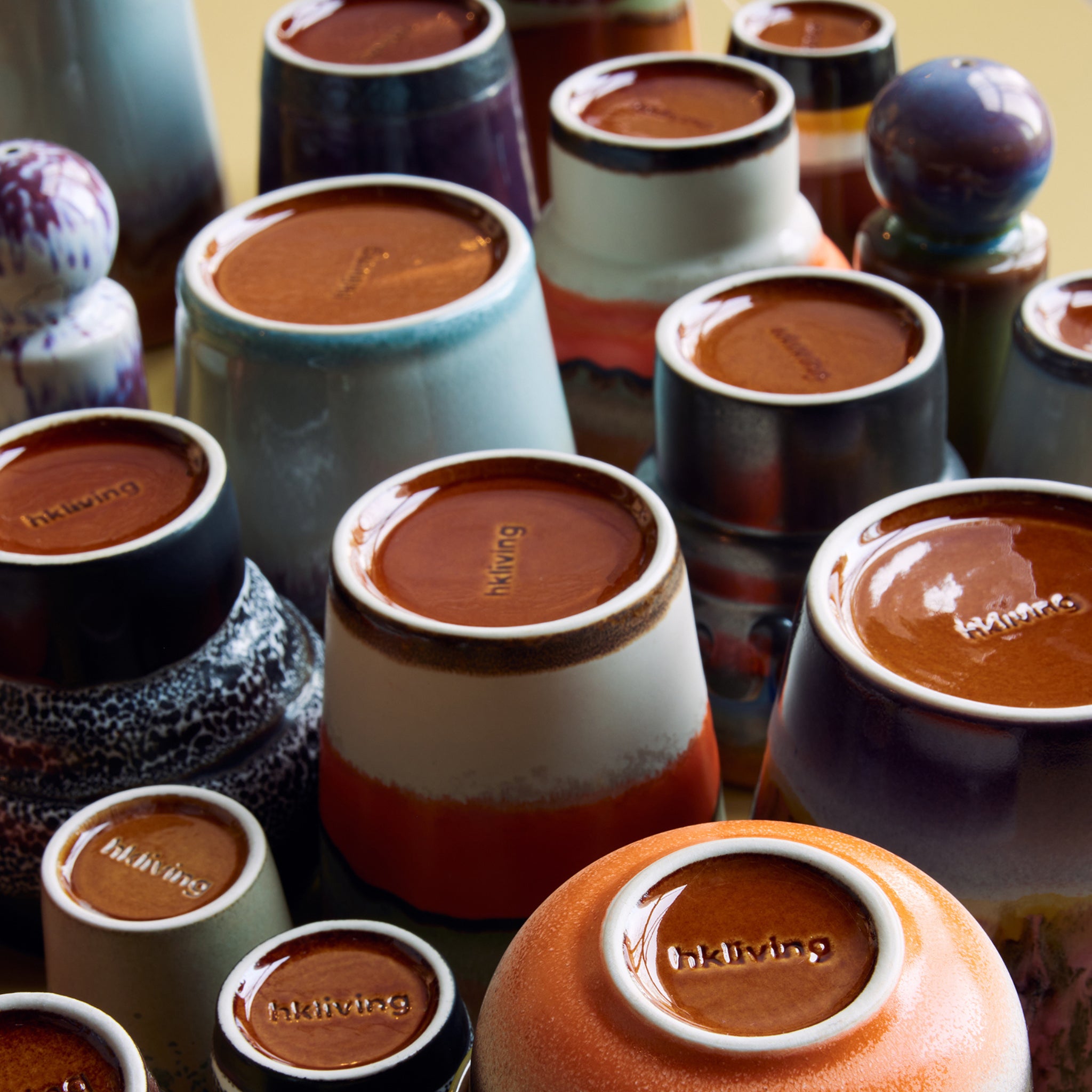 Een set HK Living 70s Ceramics Koffiemok Grounding mokken staat ondersteboven en onthult glanzende bruine bodems met het opschrift "bklynclay". Deze keramische mokken hebben verschillende patronen, glazuren en maten van het merk HK Living.