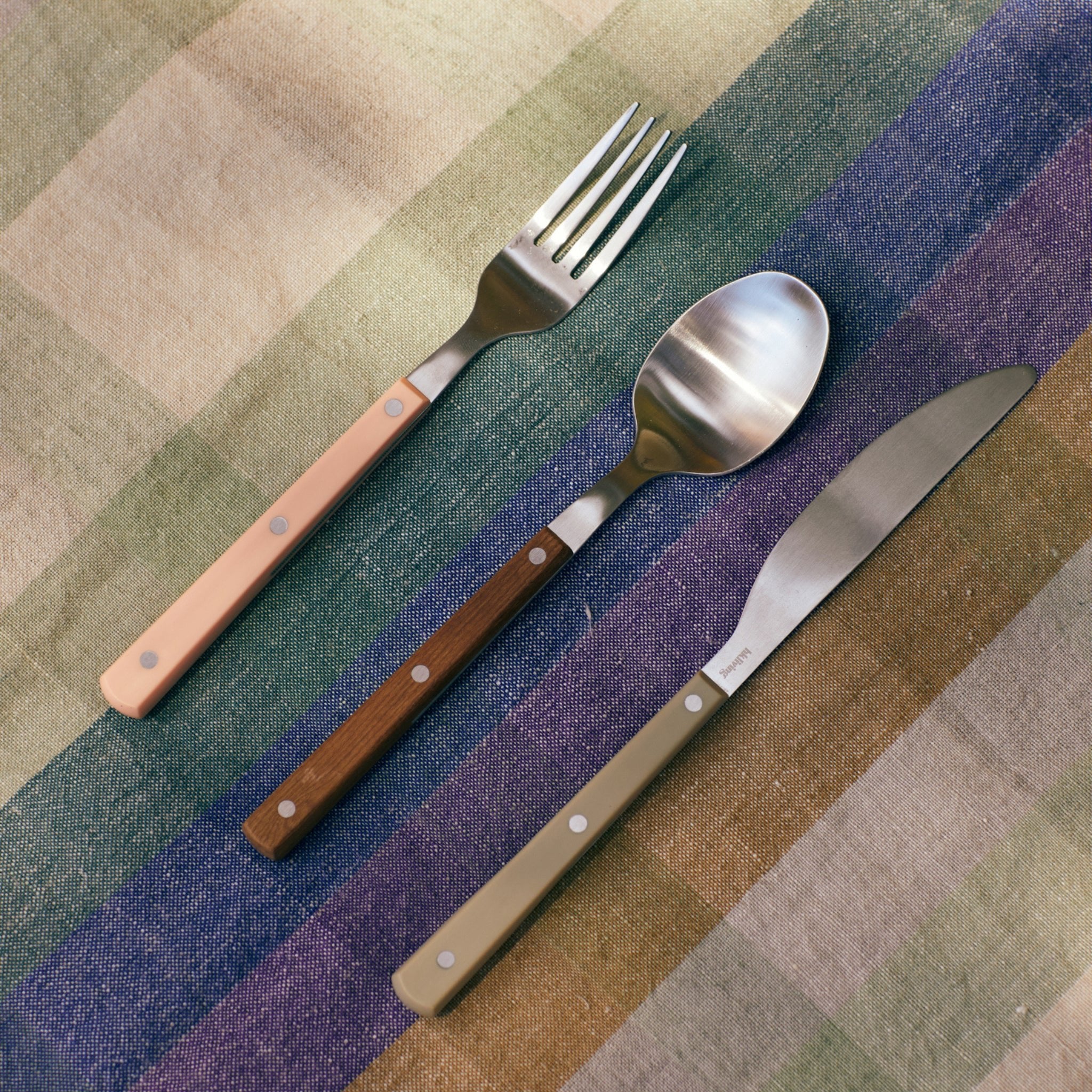 De HK Living 70s Dessertlepel Perzik, met een kleurrijk handvat, is netjes gerangschikt op een veelkleurig gestreept tafelkleed.