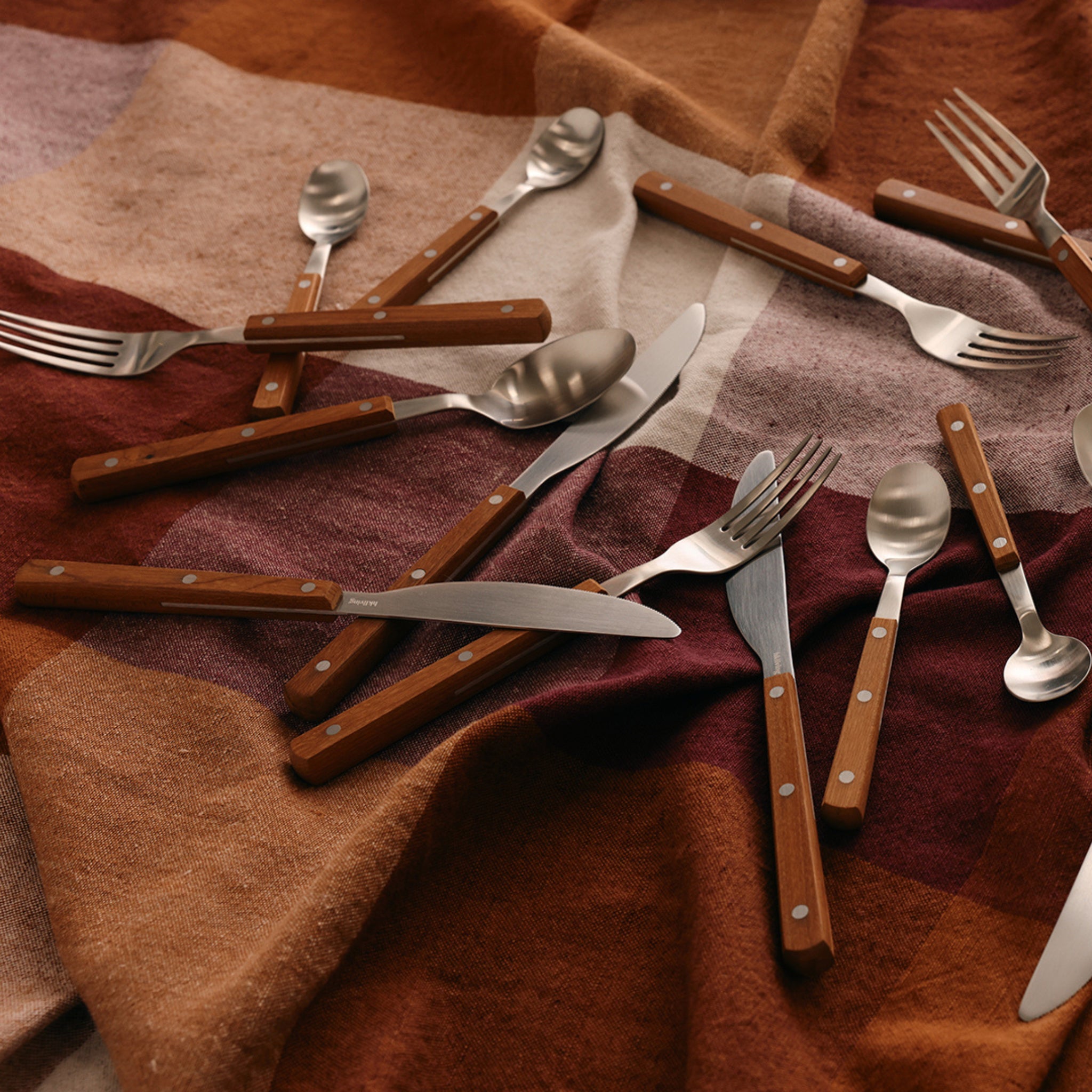 Een set HK Living 70s Cutlery tafellepels met houten handgrepen is verdeeld over een bruin en roest geruite stof, die de retro charme en vintage stijl van 70s bestek weerspiegelt.