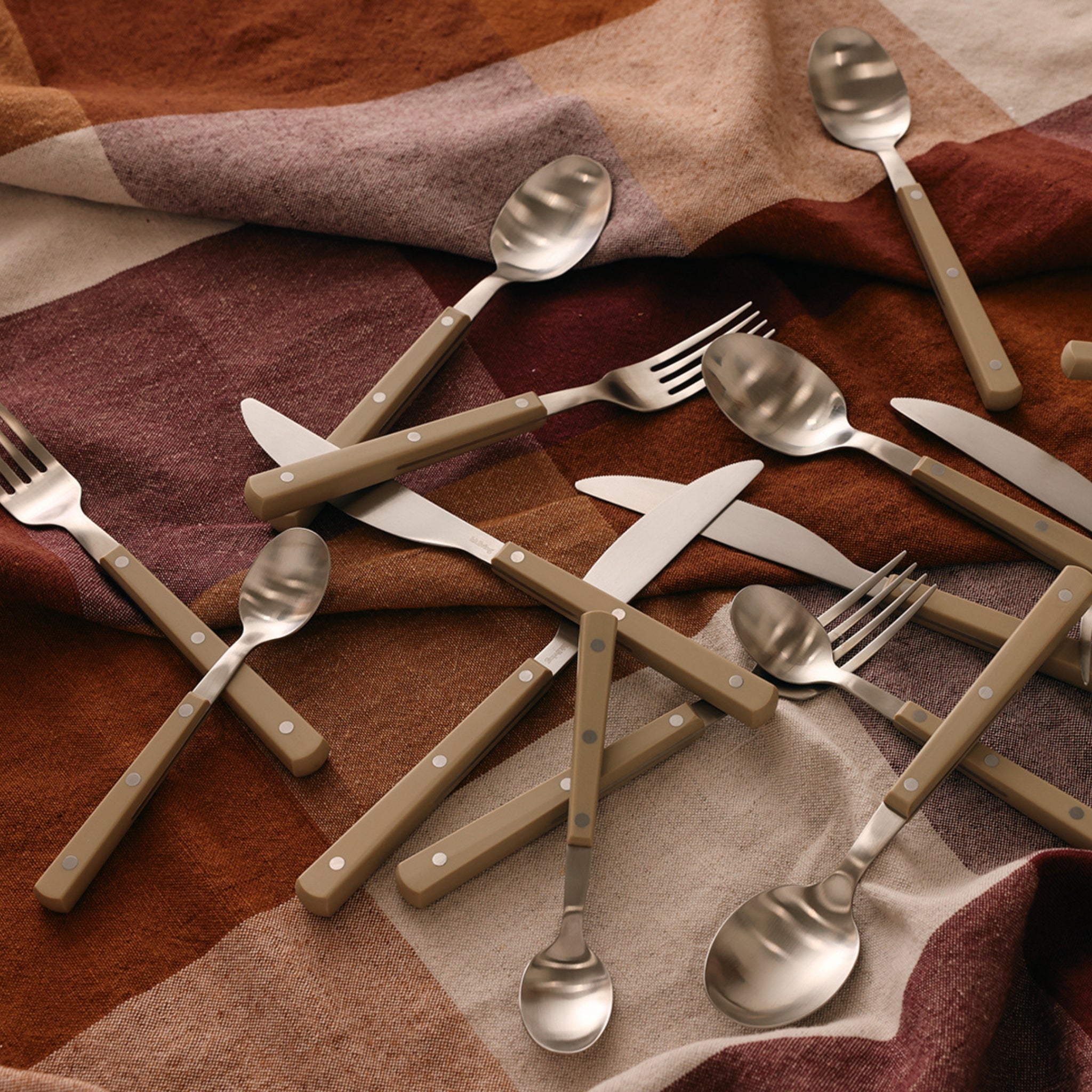 Een HK Living 70s Cutlery tafelmes in olijfgroen rust op een zachte, geruite stof in warm bruin en beige, wat de retro uitstraling van dit stijlvolle HK Living mes benadrukt.