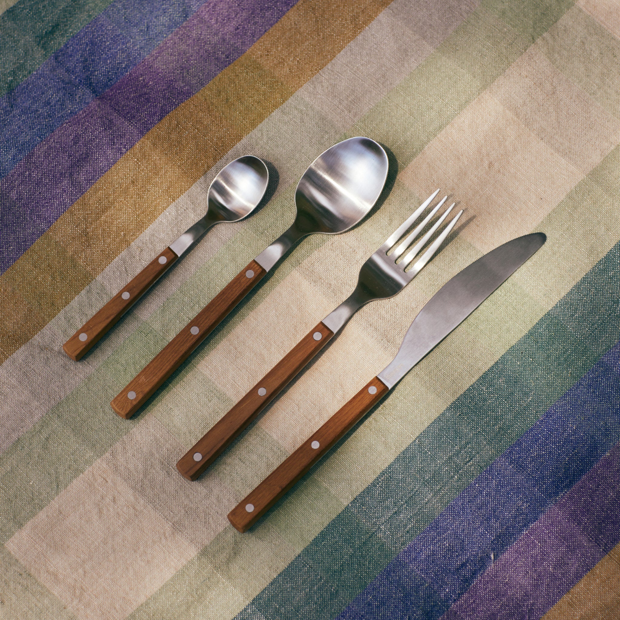 Het HK Living 70s Bestek Tafelvork Hout, met houten handvat, benadrukt de retro charme van HK Living geïnspireerd op jaren '70 ontwerpen wanneer het op een levendig gestreept doek wordt geplaatst.