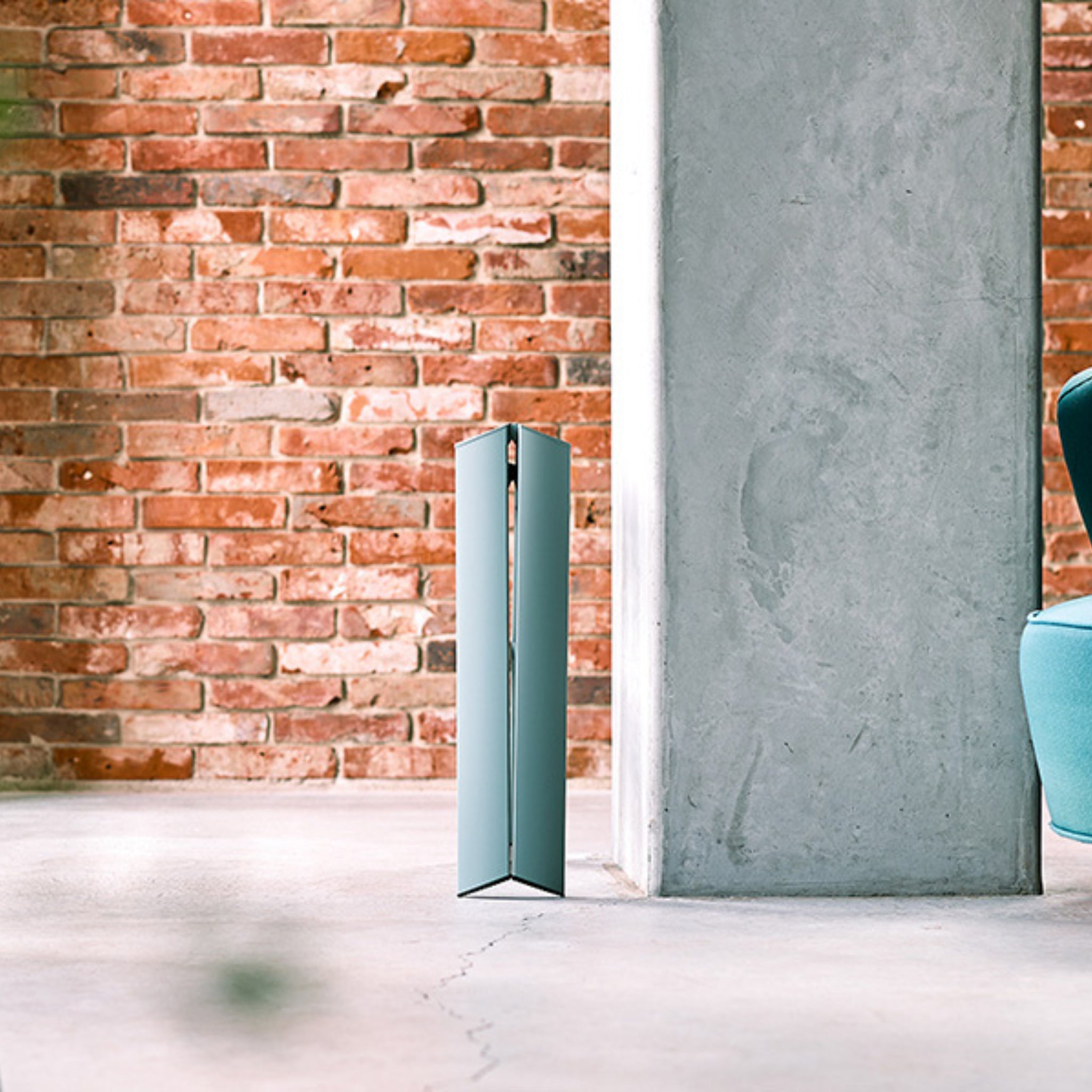Een slanke Hasegawa Lucano Ladder 2 Step in Dusty Mint van Hasegawa staat bij een betonnen pilaar in een lichte kamer met zichtbare bakstenen en een groenblauwe stoel en weerspiegelt de verfijnde Japanse designgevoeligheid.