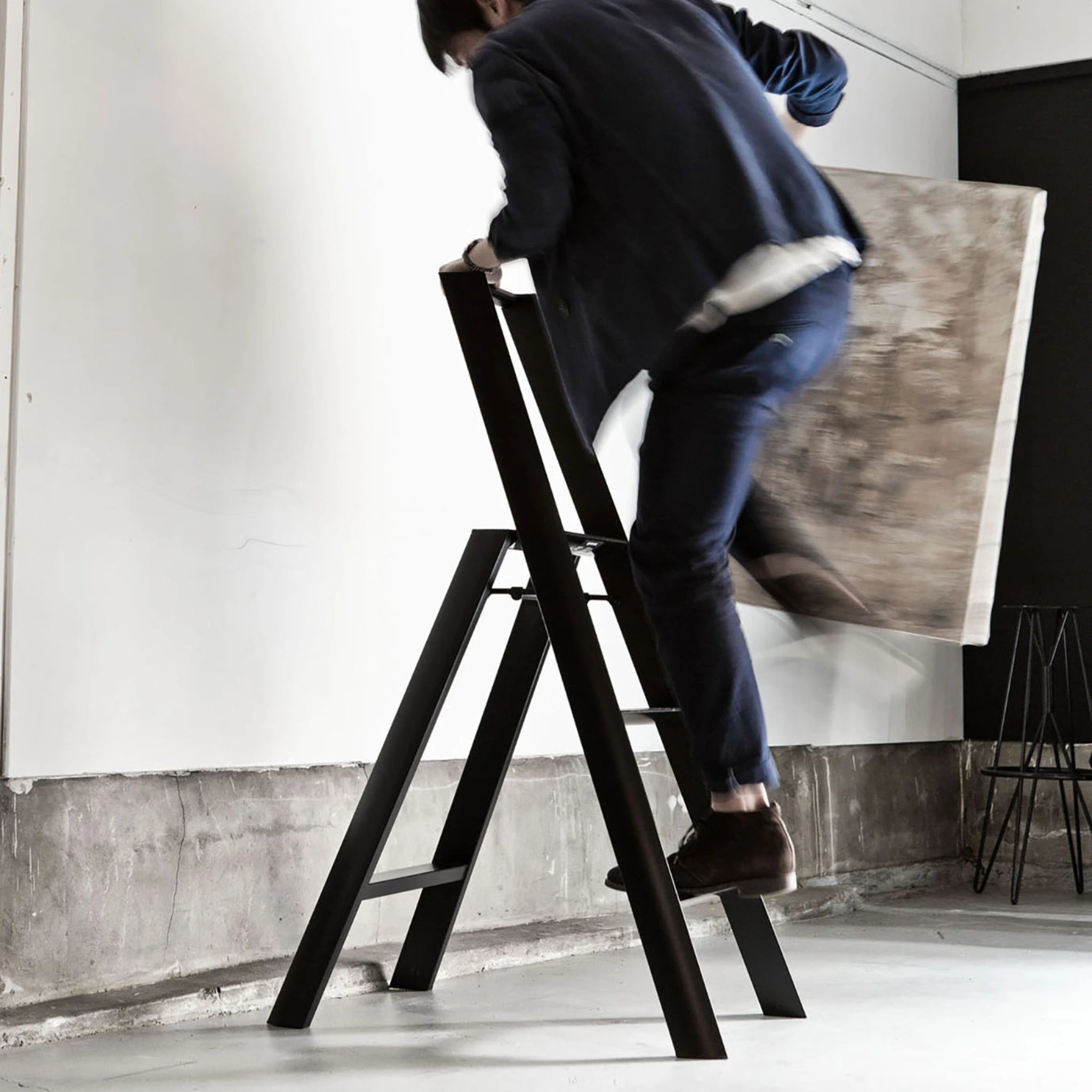 In marine draagt iemand de Hasegawa Lucano Ladder 3 Step Zwart van Hasegawa om een grote ingelijste foto op te hangen of te verwijderen in een moderne, minimalistische ruimte geïnspireerd door Japans design.
