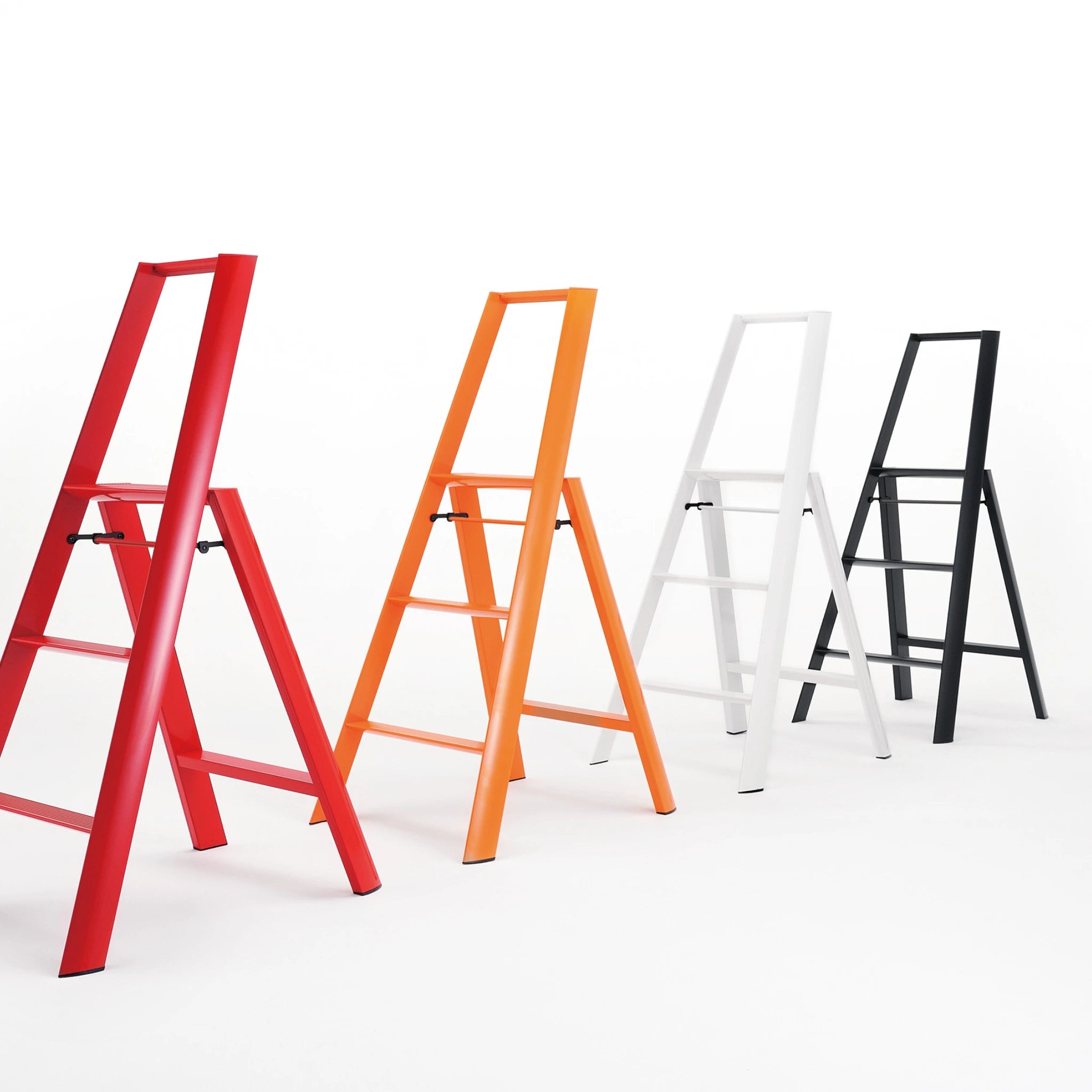 Vier moderne Hasegawa Lucano 3 Step ladders in rood, oranje, wit en zwart staan op een rij tegen een witte achtergrond. Het gedurfde zwarte ontwerp van Hasegawa voegt een opvallend contrast toe aan de minimalistische Japanse stijl van deze collectie.